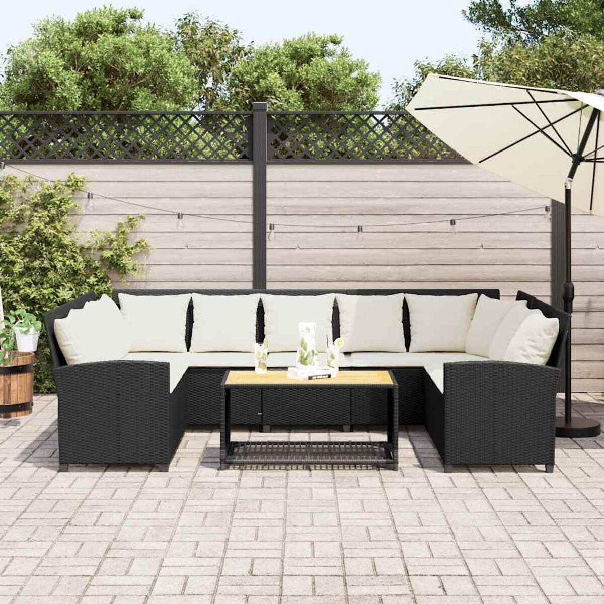 Set da patio esterno con mobili in vimini neri, cuscini bianchi e un ombrello beige.