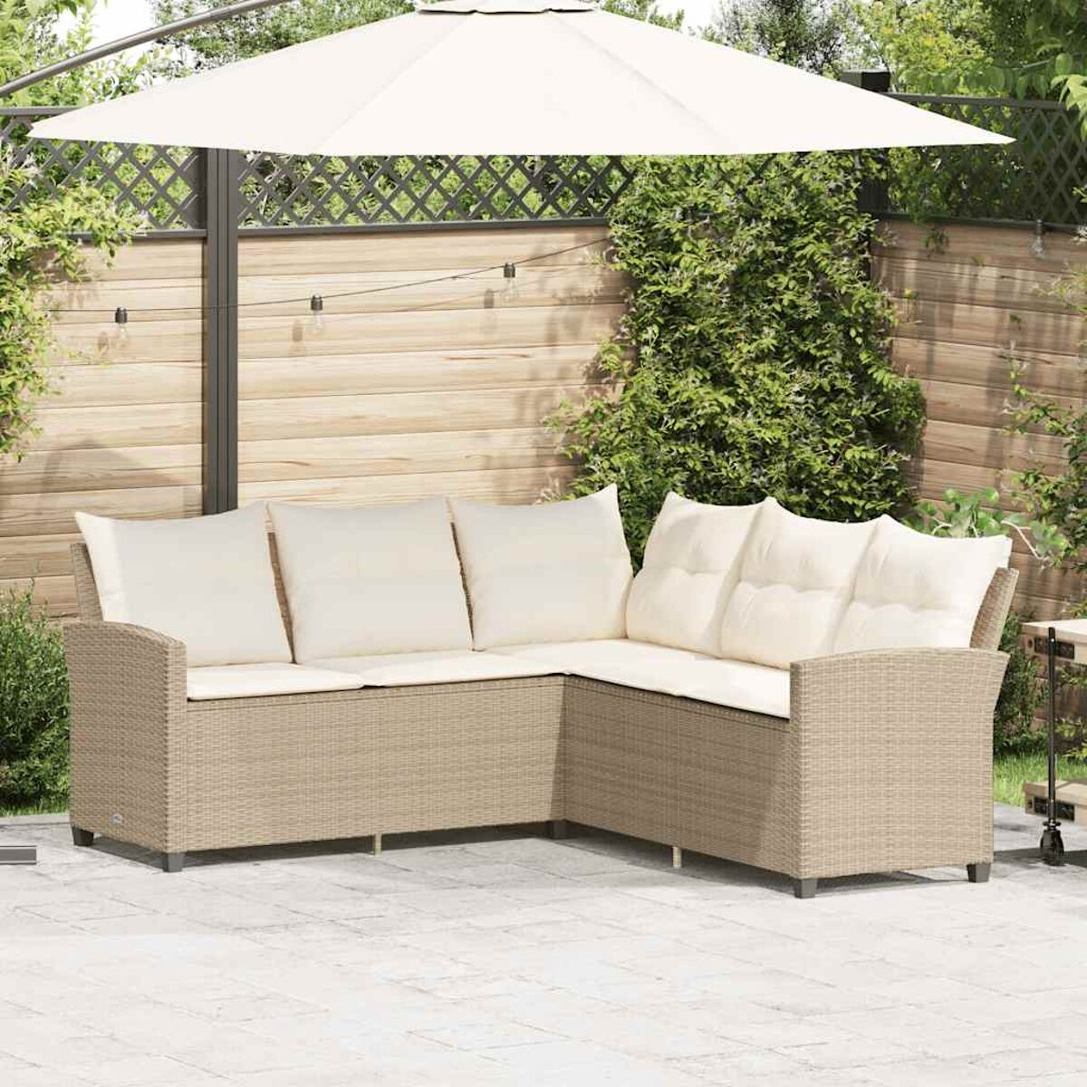 Divano angolare in vimini beige con cuscini color crema sotto un ombrellone bianco in giardino.
