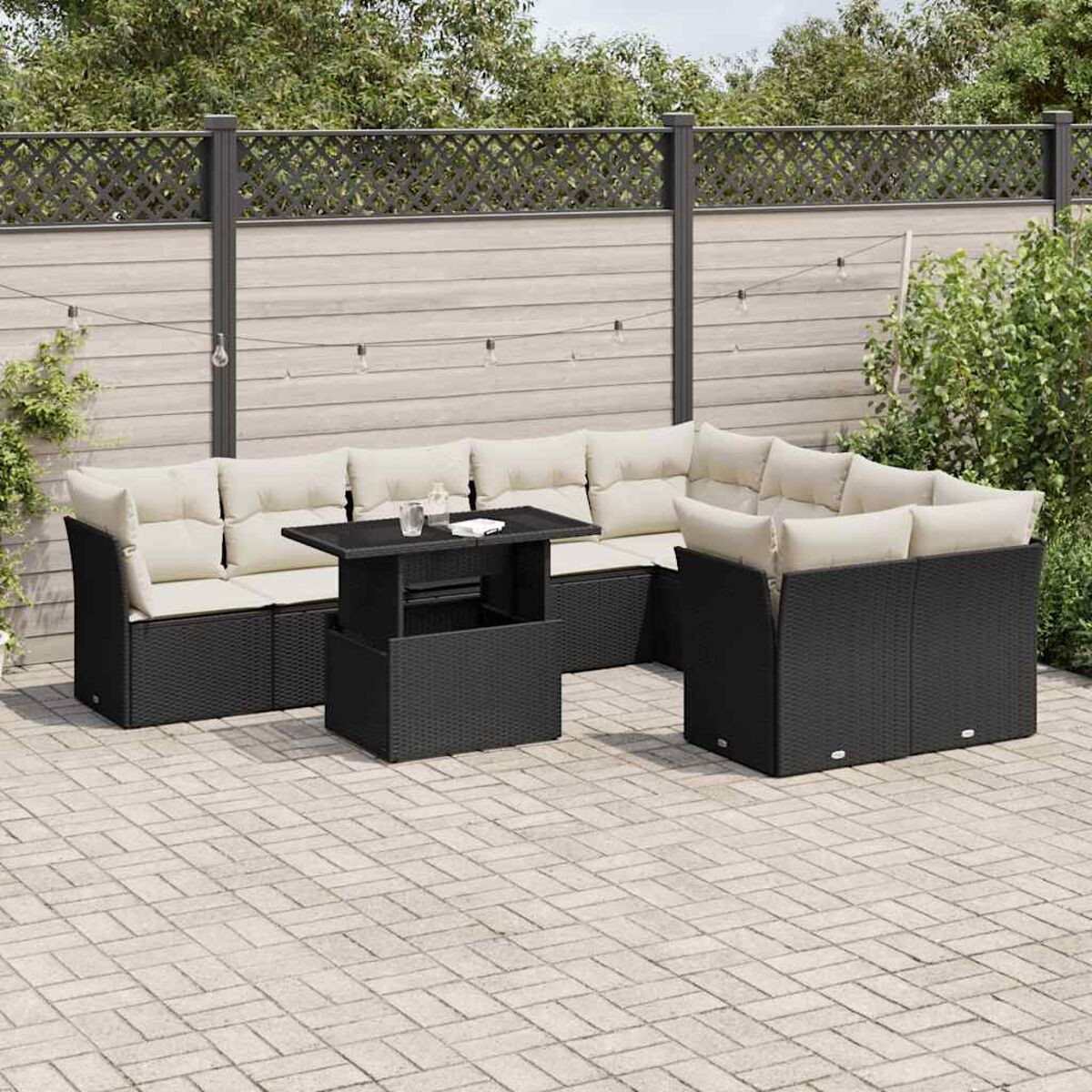Set patio esterno con mobili in vimini neri, tavolo e cuscini chiari, e pavimento in mattoni.