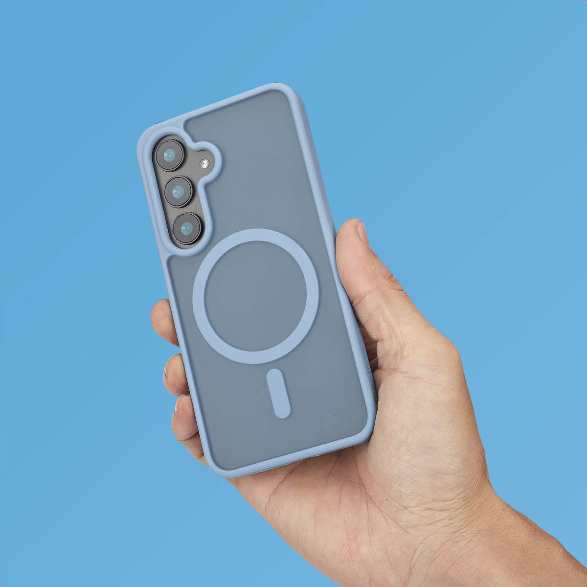 Main tenant une coque bleue avec cercle MagSafe et trois objectifs, sur fond bleu.