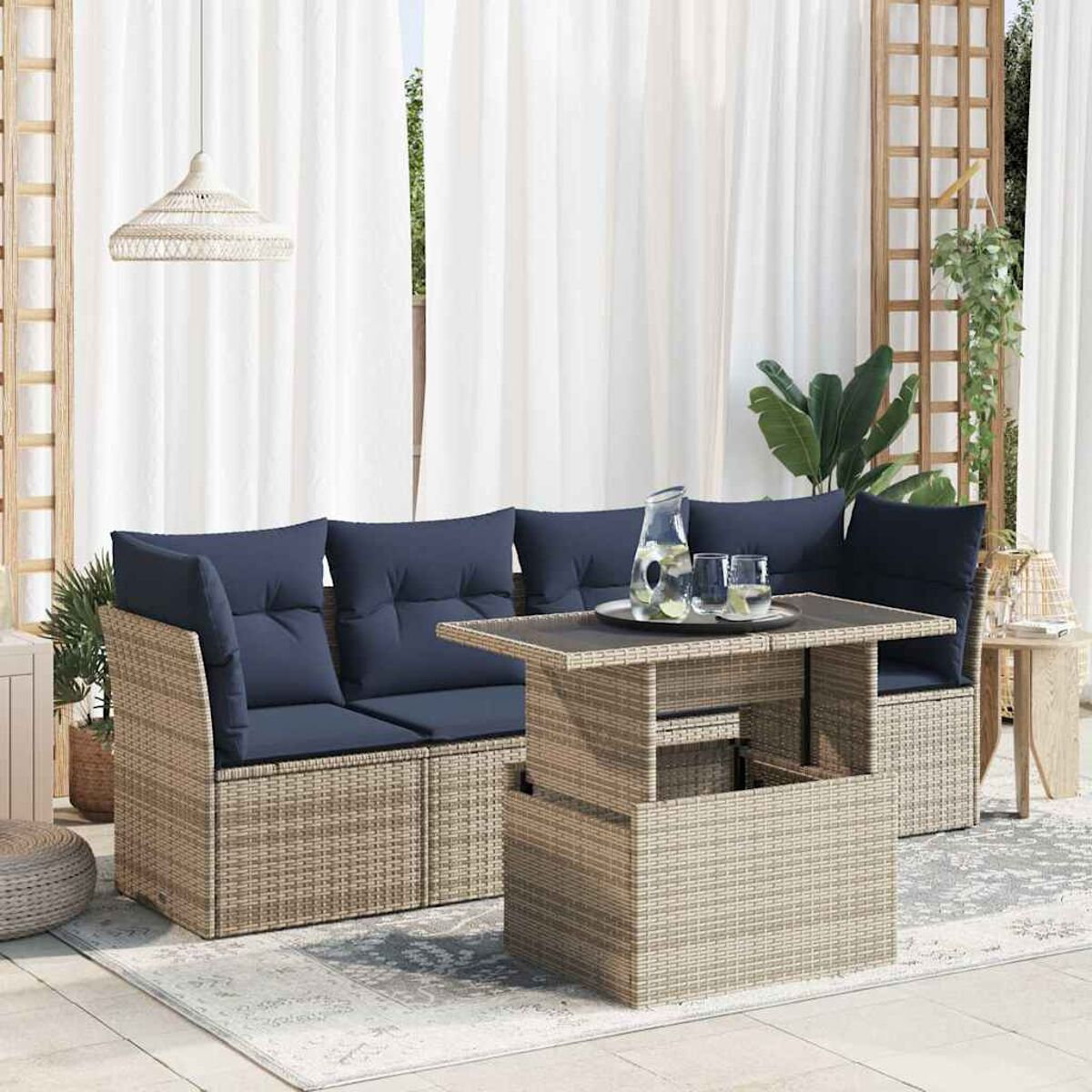 Divano esterno in vimini beige con cuscini blu navy, tavolo sollevabile e tende bianche.