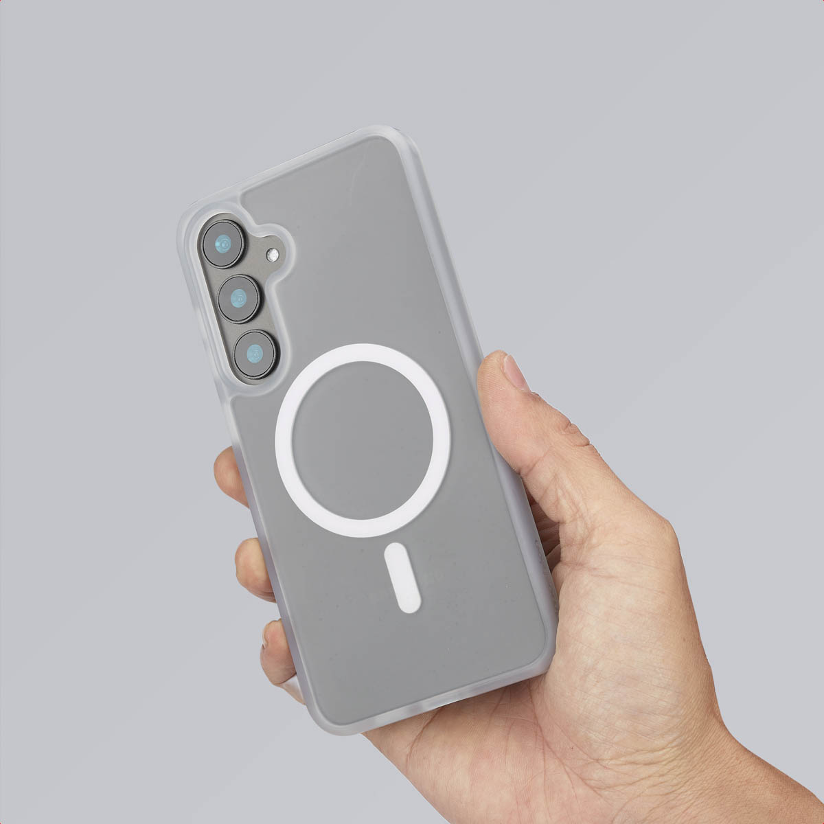Een hand die een telefoonhoes vasthoudt met een witte cirkelvormige magneet op een grijze achtergrond.