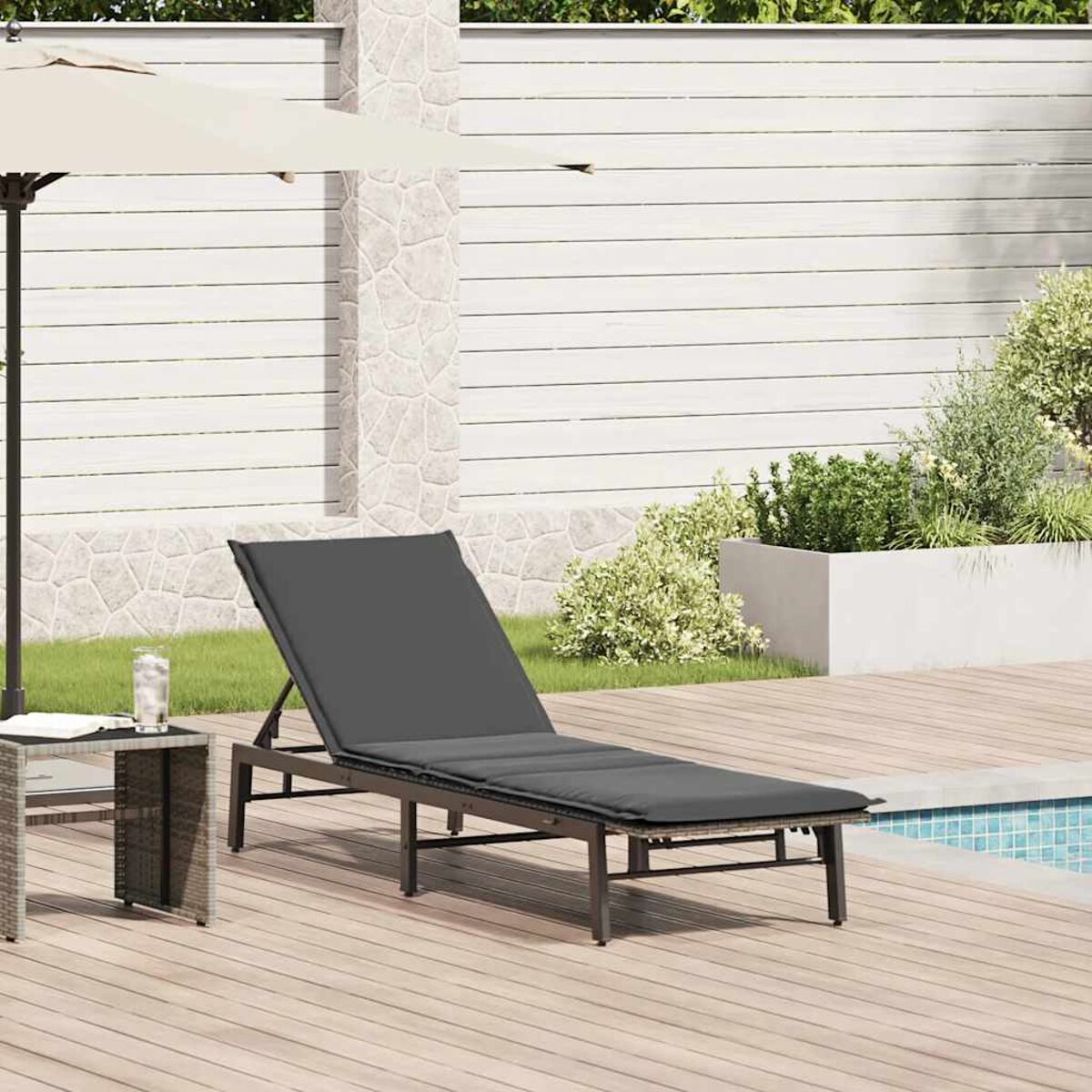 Eine graue Sonnenliege mit einem Glas Wasser und einem Beistelltisch neben einem Pool.