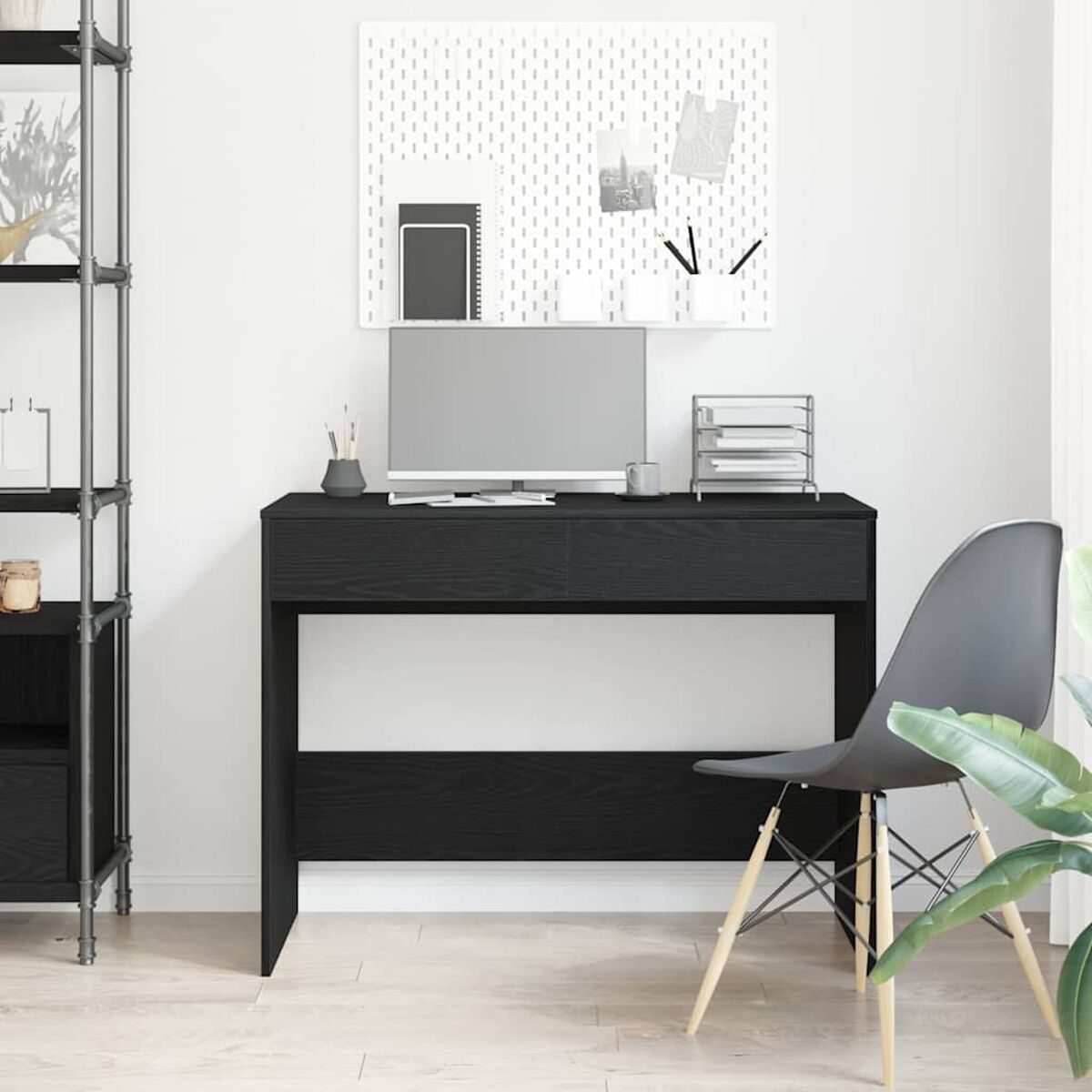 Ein schwarzer Schreibtisch mit Computer, Stuhl und Dekoration. Eine Lochwand hängt an der weißen Wand.
