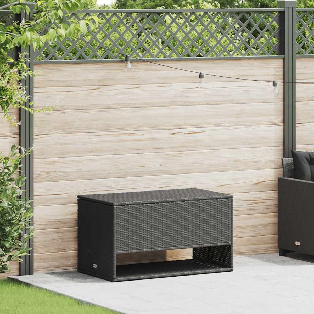 Schwarze Aufbewahrungstruhe aus Korbgeflecht mit unterem Regal auf einer Terrasse mit Holzzaun.