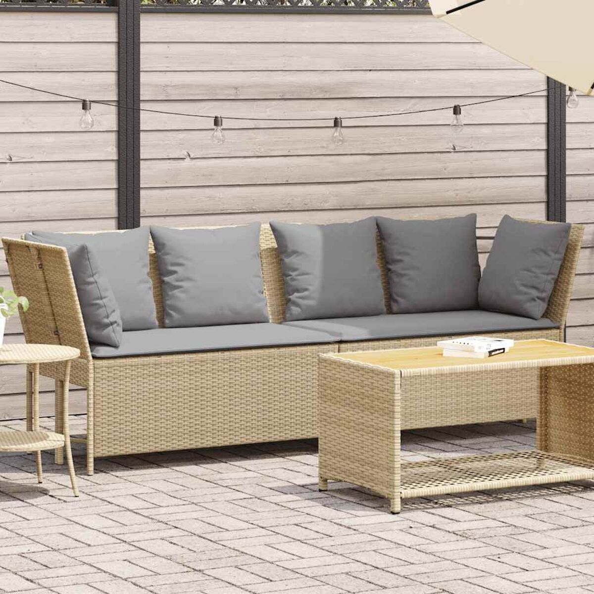 Divano in rattan beige con cuscini grigi e tavolo su un patio, scena all'aperto.