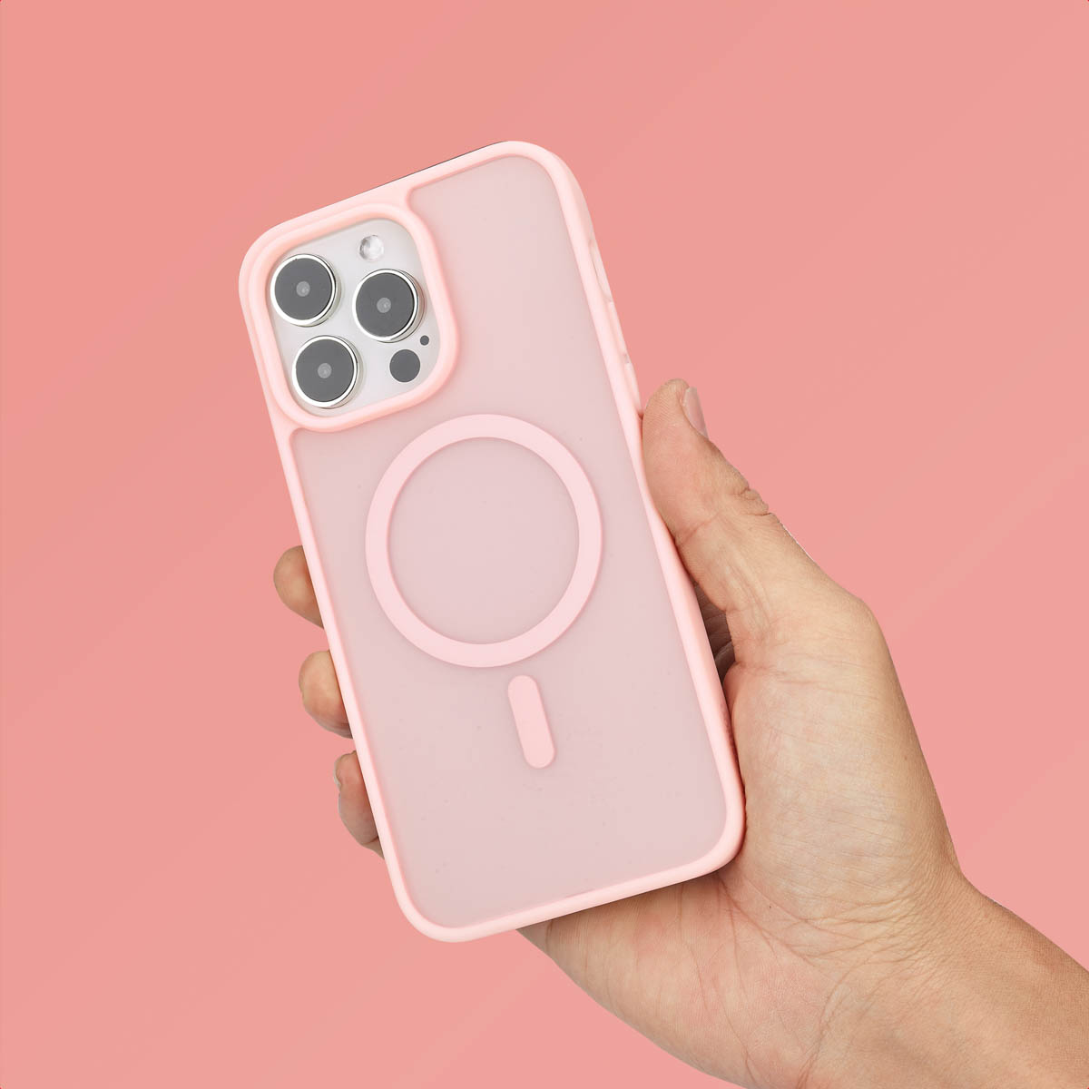 Main tenant une coque de téléphone rose avec un cadre rose. La coque a un anneau MagSafe.