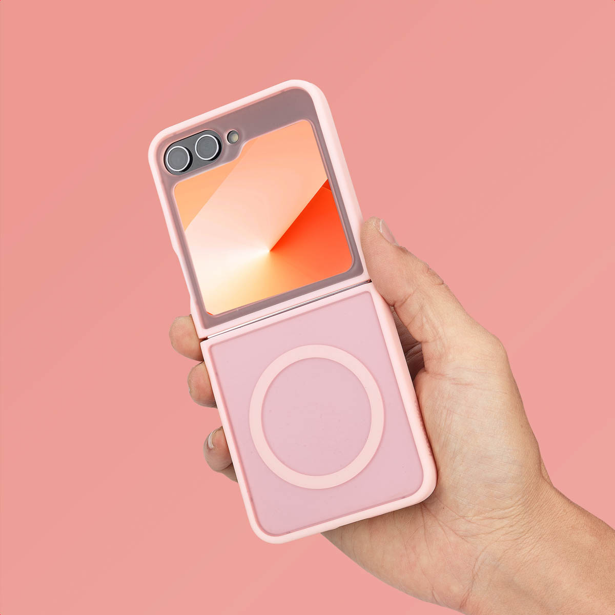 Een hand houdt een roze telefoonhoes met een MagSafe cirkel, telefoon is open, roze achtergrond.
