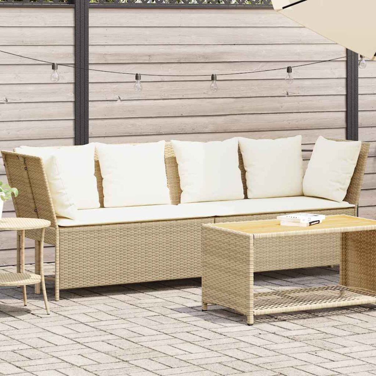 Divano da esterno in vimini beige con cuscini bianchi e un tavolino in legno.