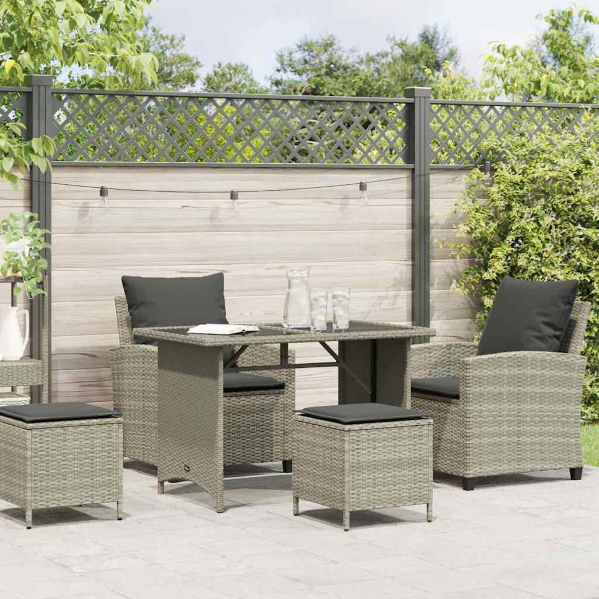 Set da patio esterno grigio con tavolo, sedie e pouf su un patio in pietra con vegetazione.
