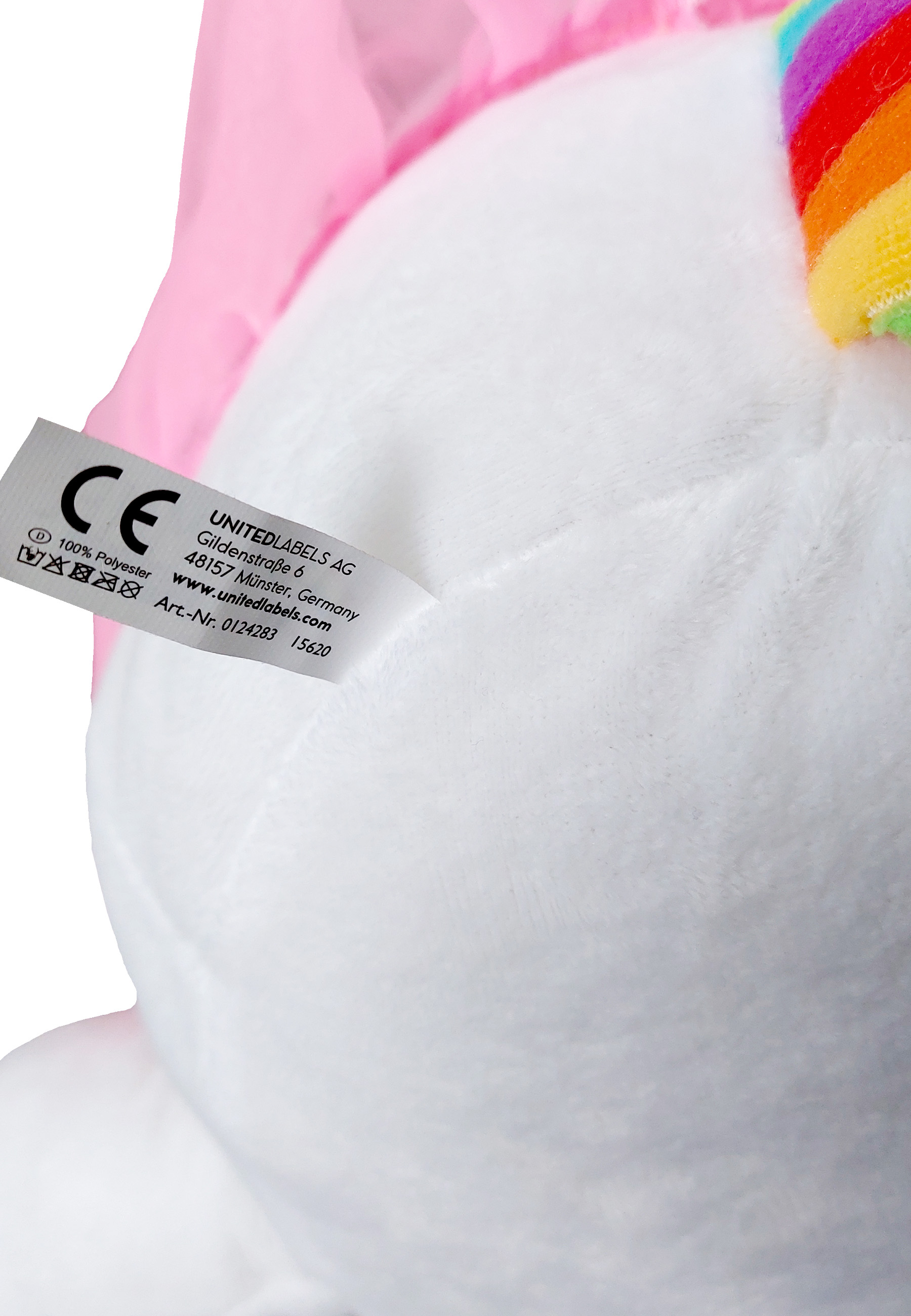 Nahaufnahme eines weißen Plüsch-Einhorn-Spielzeugs mit einem Regenbogenhorn und einem Etikett. Etikett enthält CE-Kennzeichen.