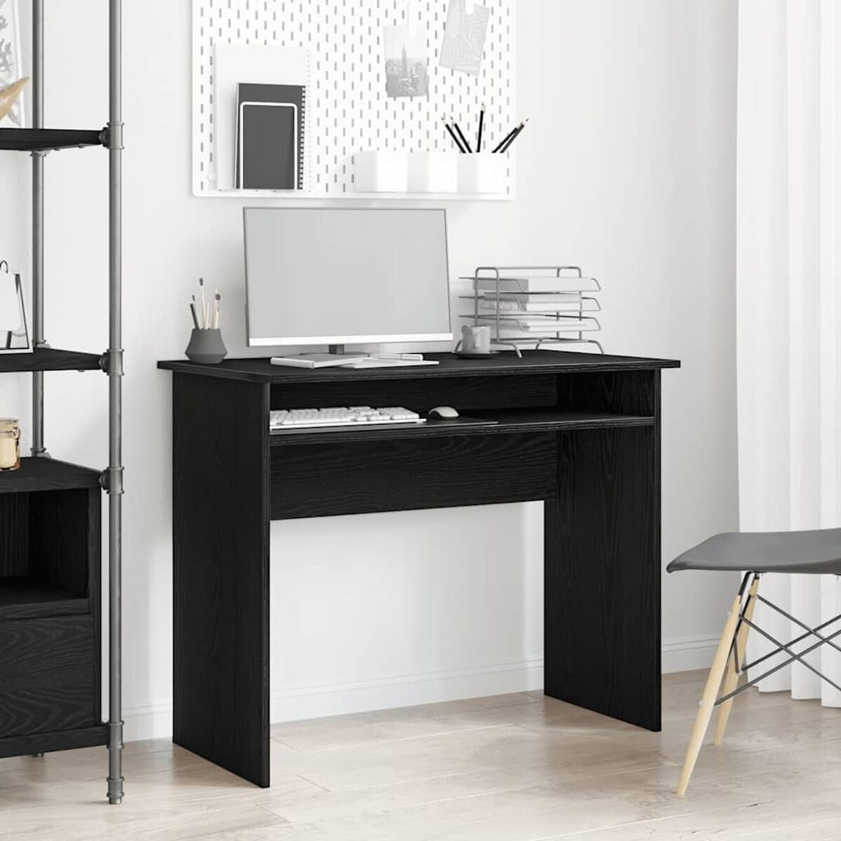 Ein schwarzer Schreibtisch mit Computer, Tastatur und Büromaterial an weißer Wand.