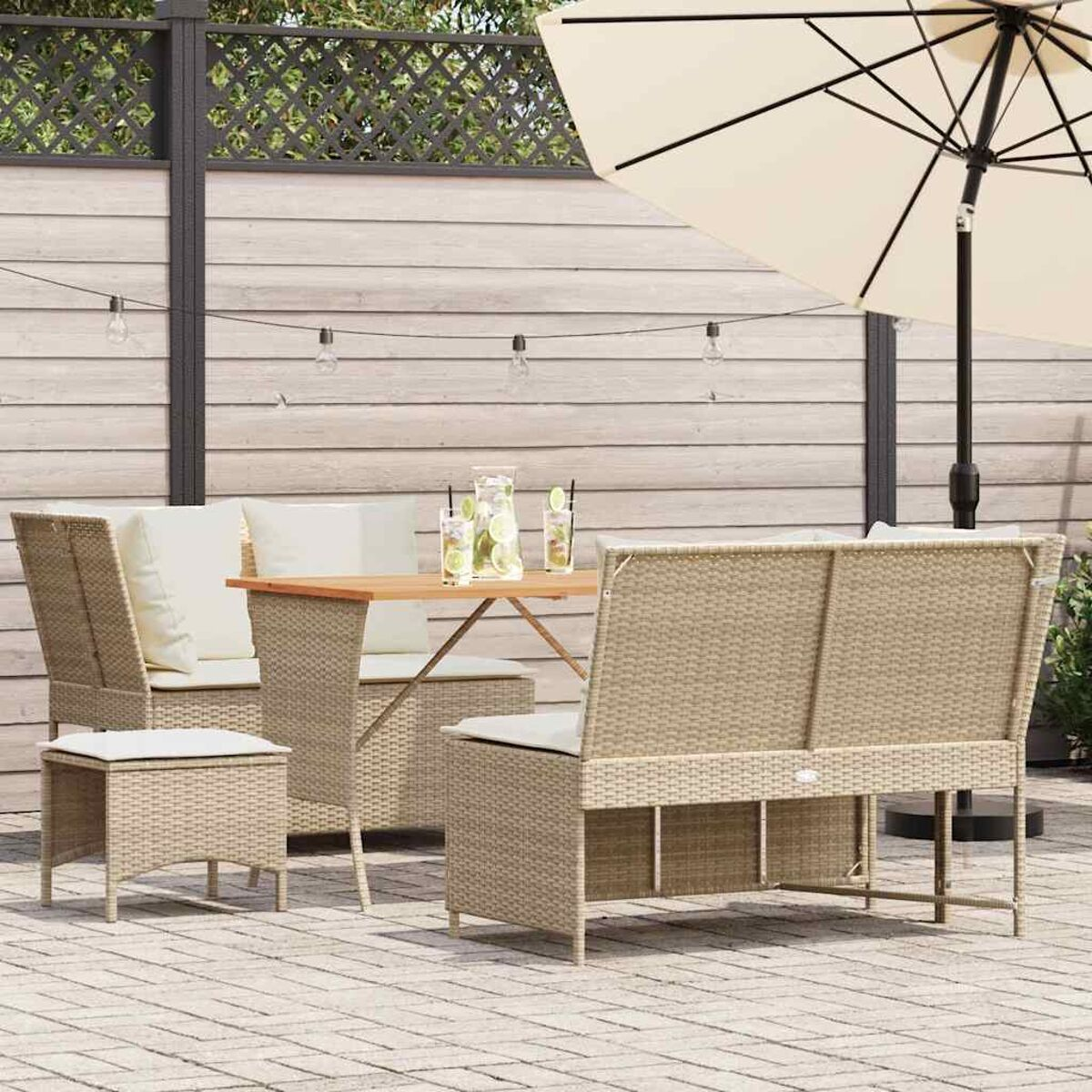 Un set da pranzo in rattan da esterno con tavolo in legno, sedie e panca, sotto un ombrello beige.