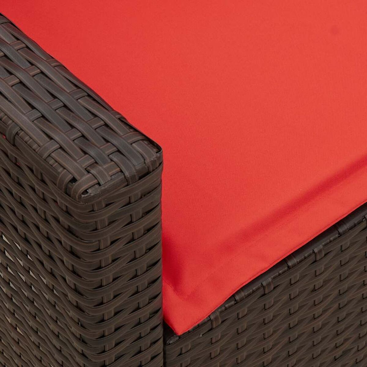 Primo piano di un angolo di divano in rattan con un cuscino rosso.