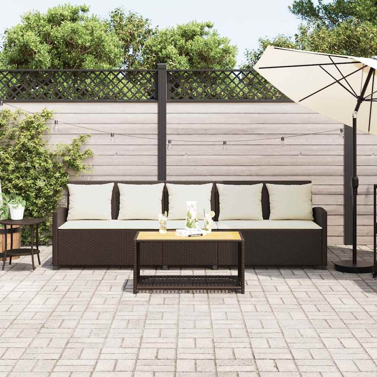 Scena del patio all'aperto: un divano in vimini marrone scuro, tavolino e ombrellone. Pavimento in mattoni e recinzione in legno sullo sfondo.