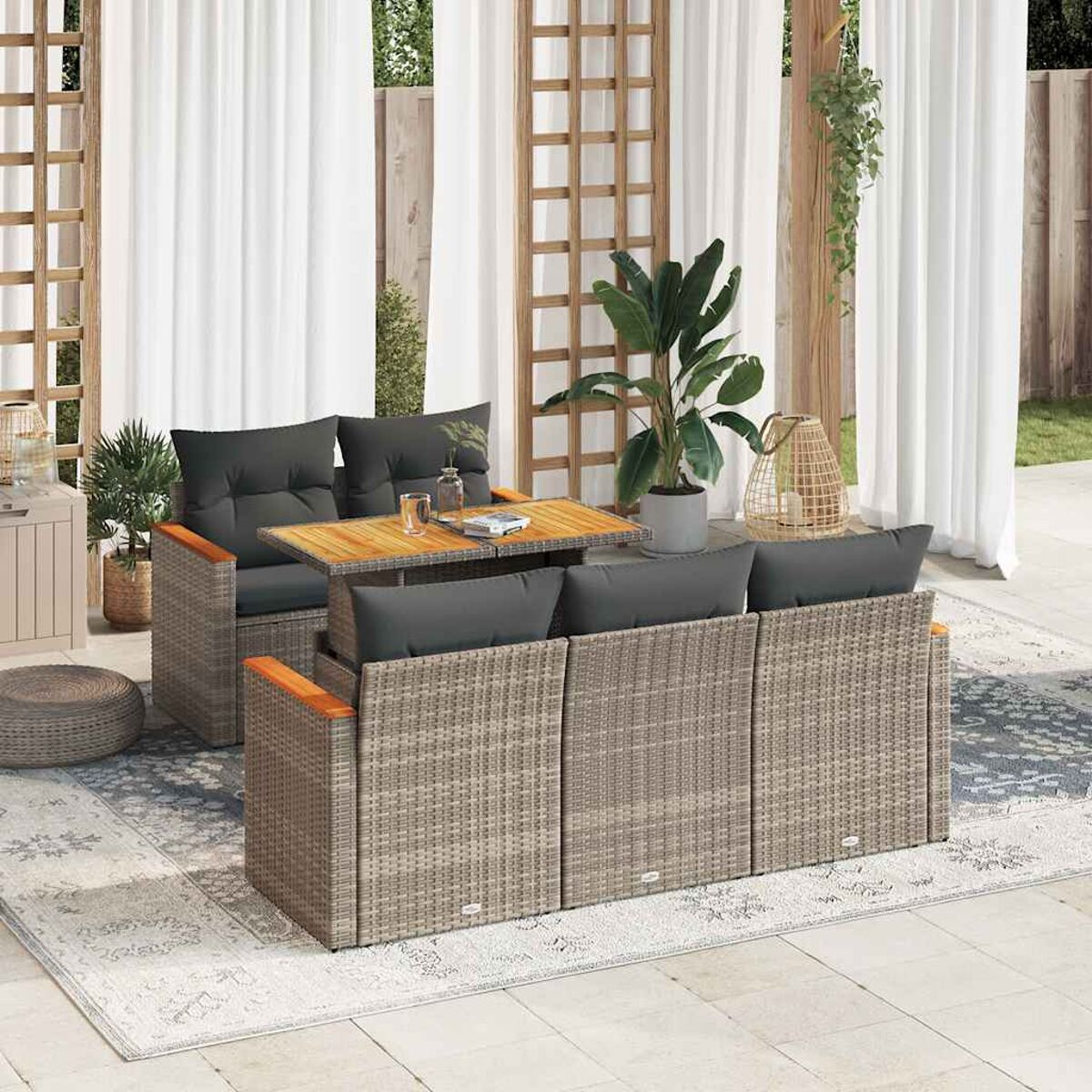 Rattan-Sofagarnitur mit Tisch. Graue Kissen, Holzarmlehnen. Weiße Vorhänge, Teppich und Pflanzen.