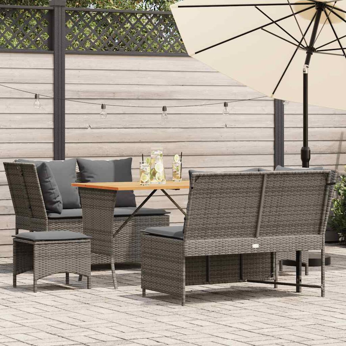 Set da patio all'aperto con tavolo, sedie e ombrellone, contro una recinzione con luci a corda.