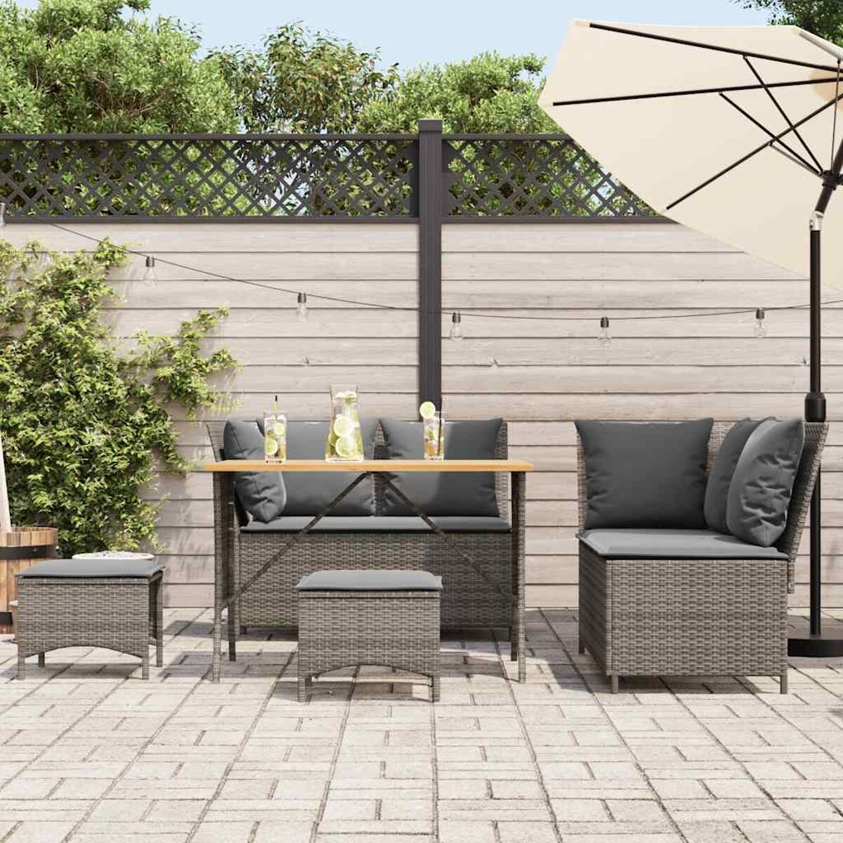 Set da patio all'aperto con mobili in vimini grigi, un tavolo e un ombrellone. Recinzione in legno sullo sfondo.