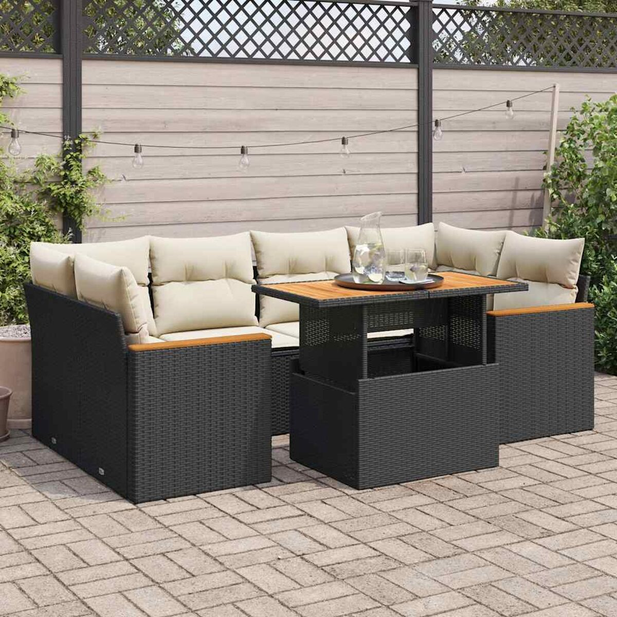 Un set da patio esterno presenta mobili in vimini nero, cuscini color crema e un piano del tavolo in legno.