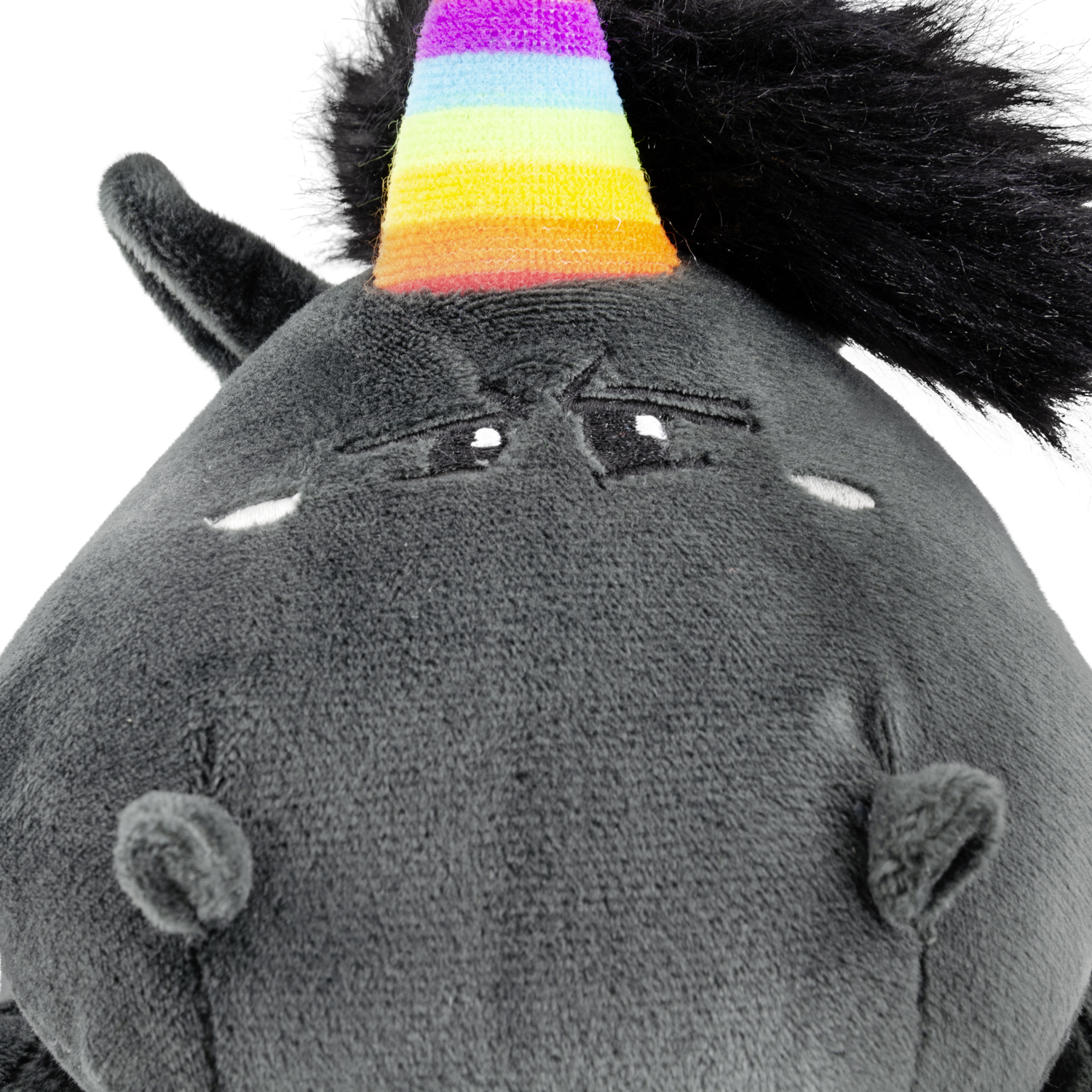Graues Einhorn-Plüschtier mit Regenbogenhorn und traurigem Ausdruck. Weißer Hintergrund.