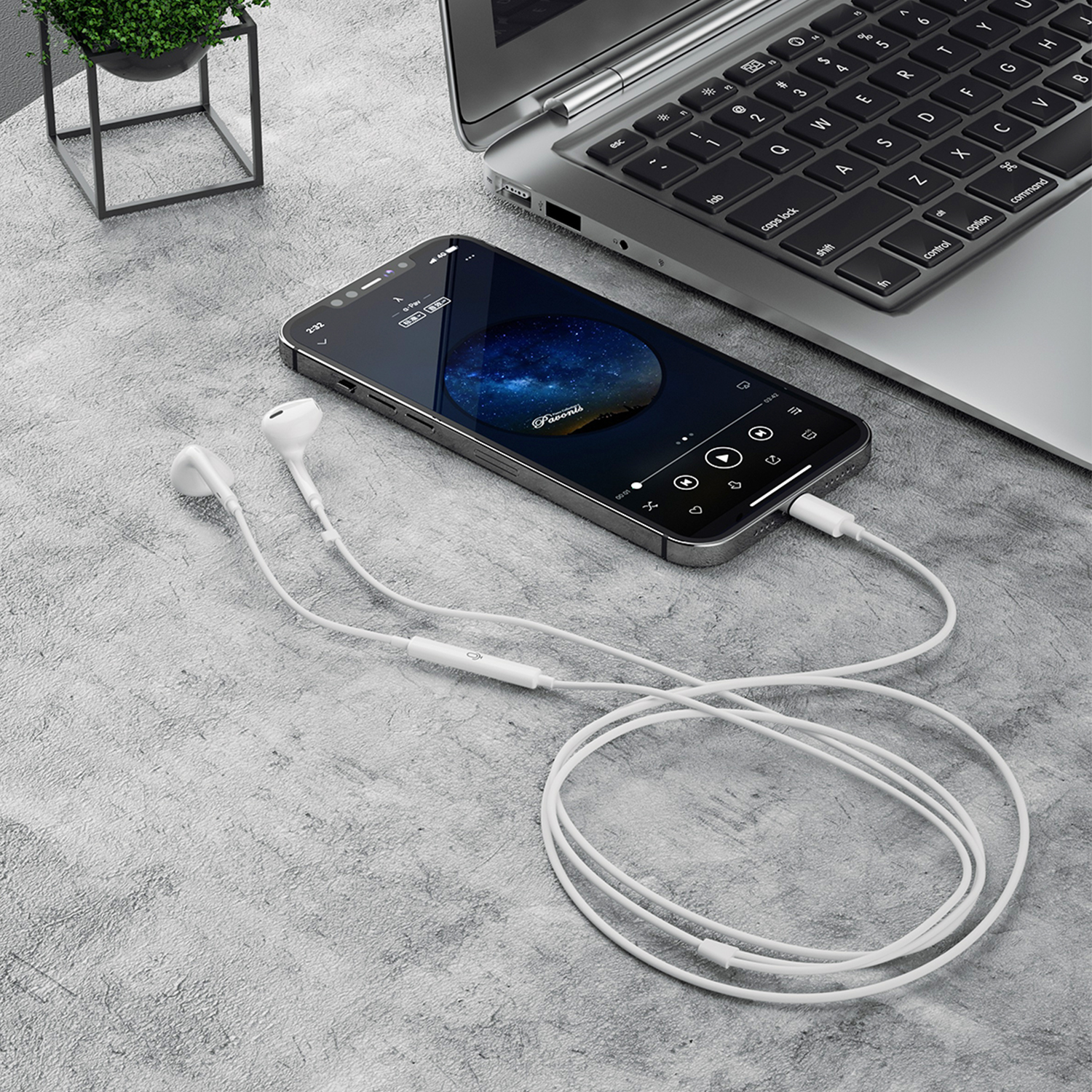 Auricolari bianchi collegati a smartphone e laptop su superficie grigia, con pianta.