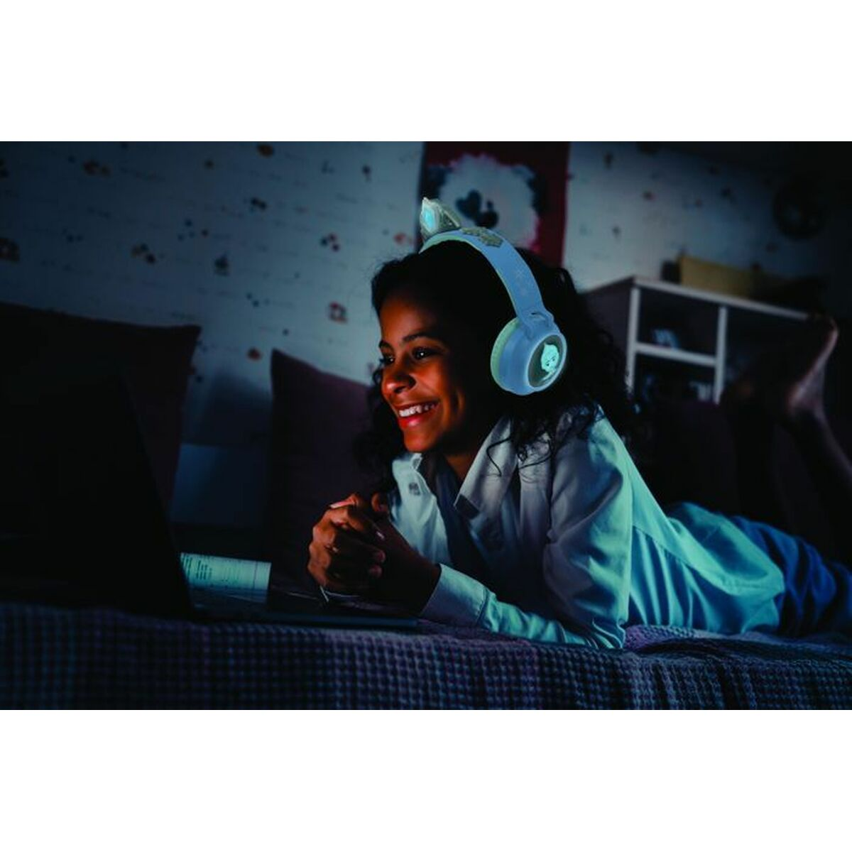 Dziewczyna w słuchawkach z uszami kota uśmiecha się do ekranu laptopa w ciemnym pokoju.