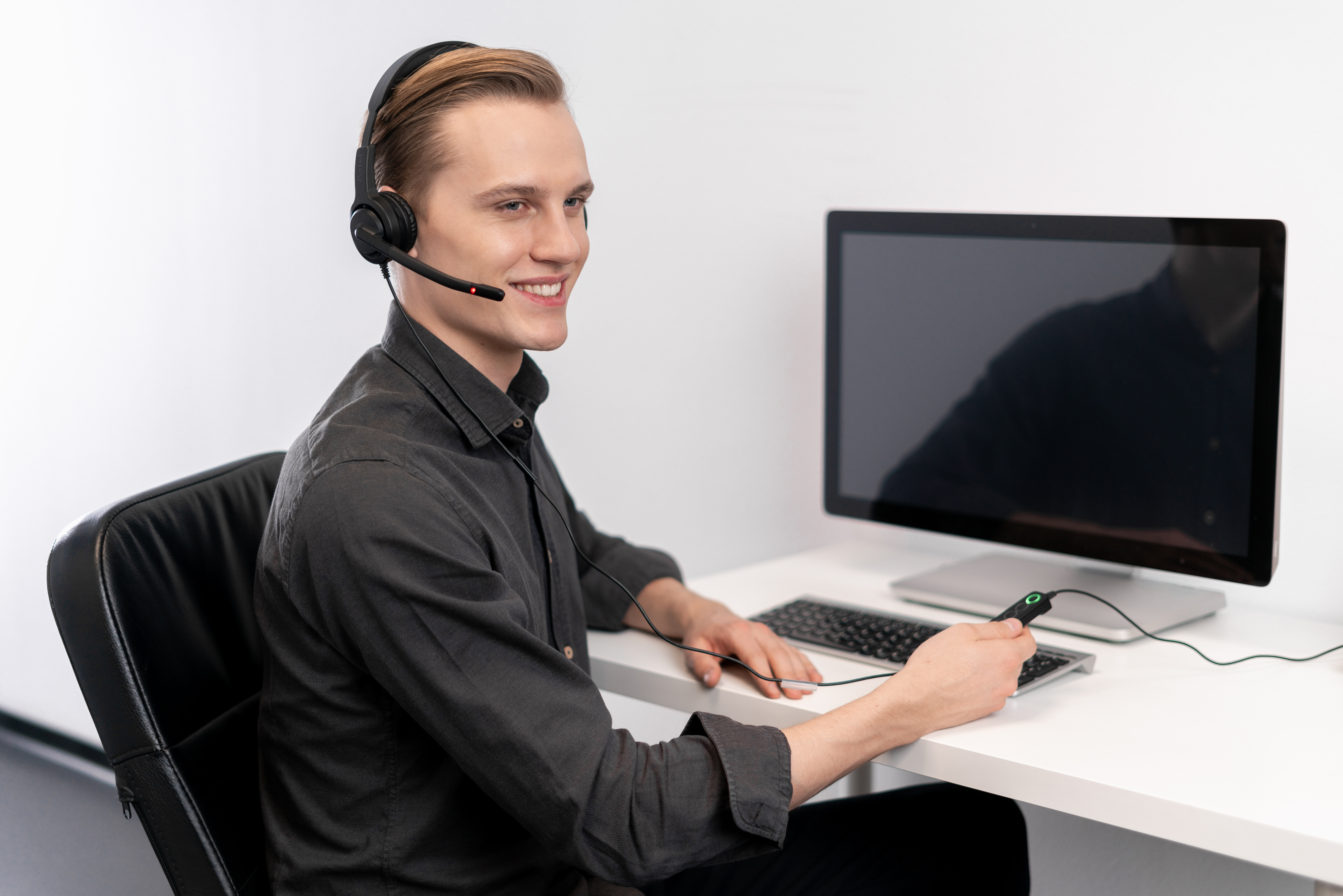 Un uomo con le cuffie sorridente, seduto a una scrivania del computer.