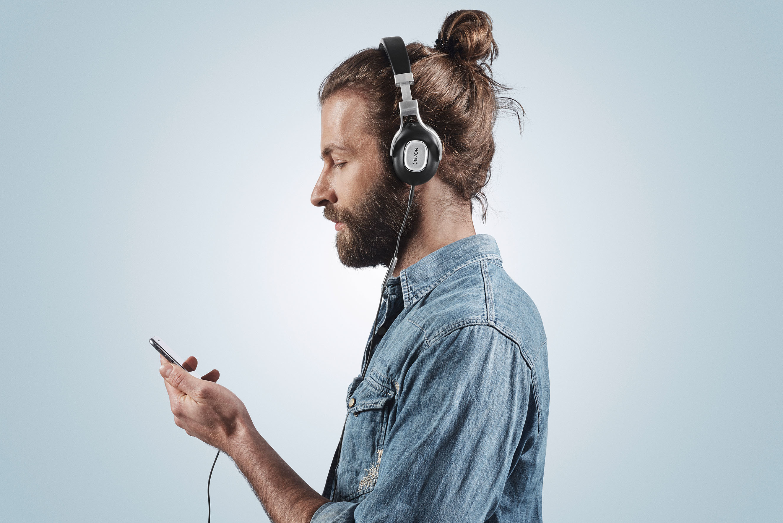 Sakalı bir adam, siyah kulaklık takmış, bir telefon tutuyor, telefona bakıyor.