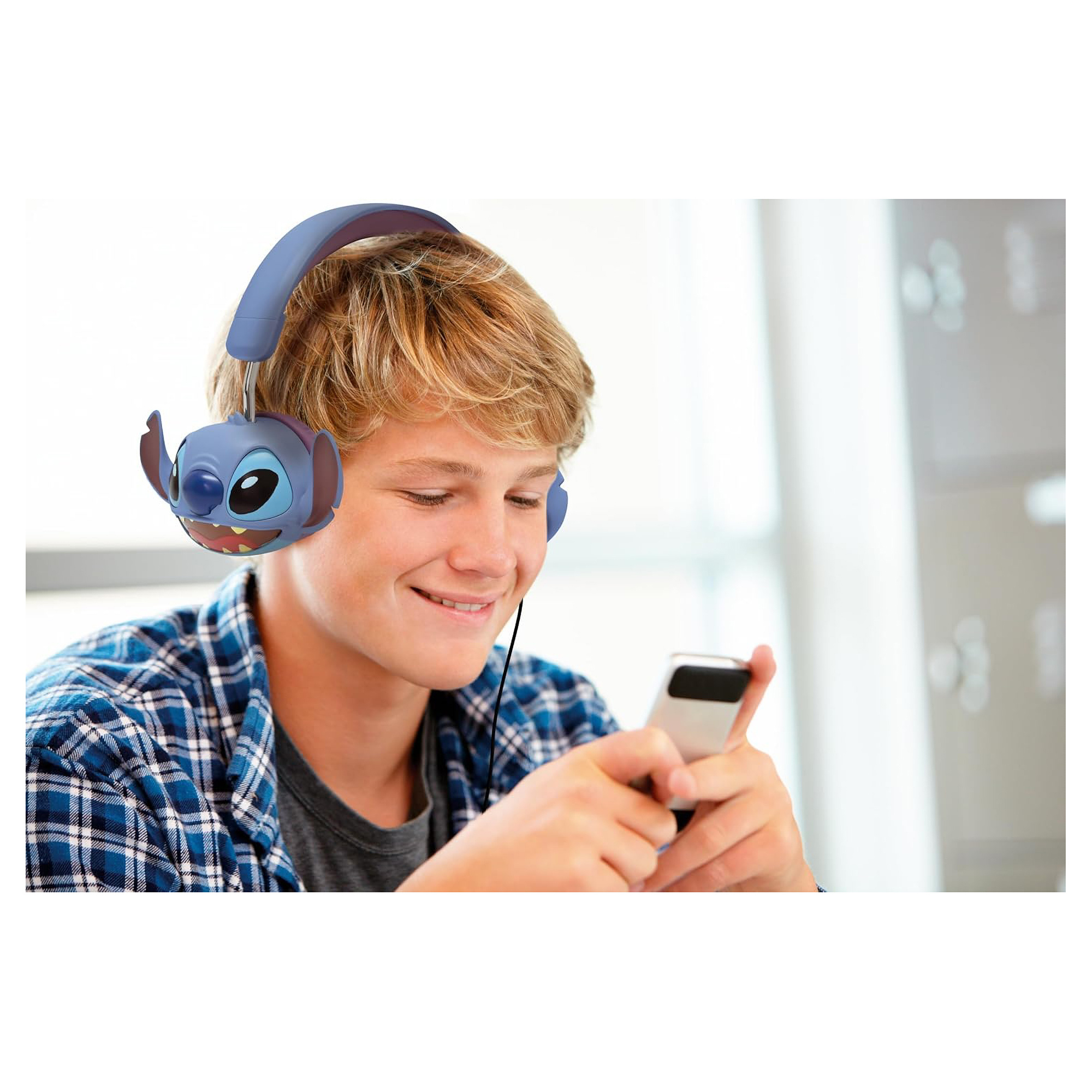 Chłopiec w słuchawkach Stitch uśmiecha się, patrząc na telefon. Tłem jest szkoła.