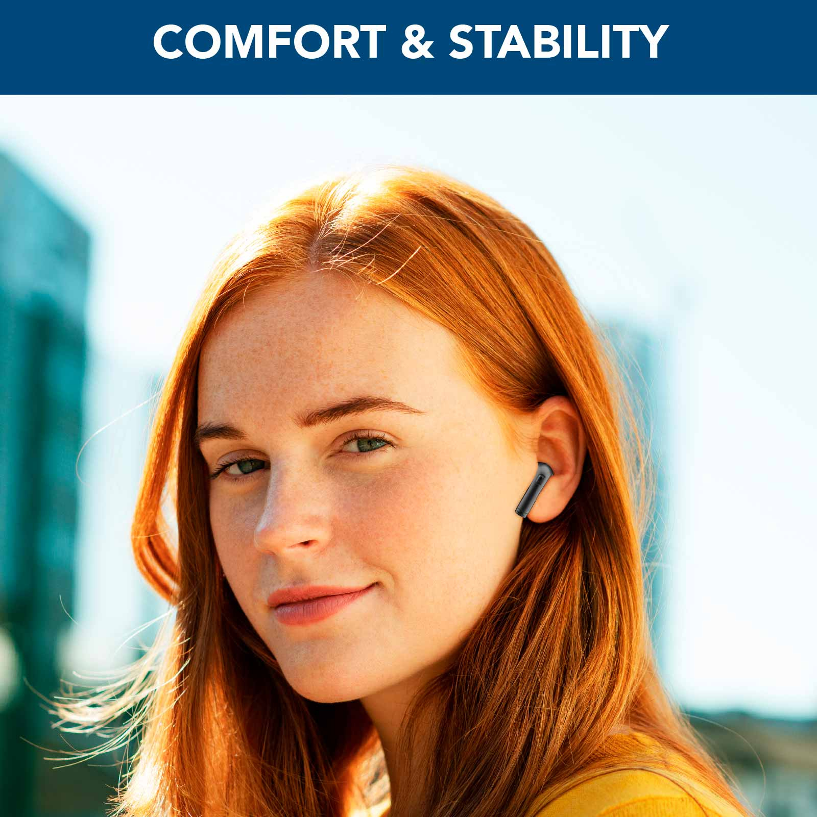 Kobieta z rudymi włosami nosząca czarne słuchawki. Tło to błękitne niebo i budynek.