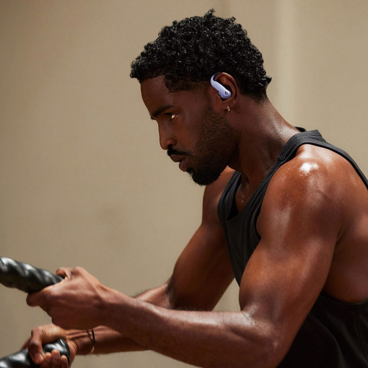 Mężczyzna w czarnym podkoszulku, który podczas ćwiczeń ma na sobie jasno fioletową słuchawkę.