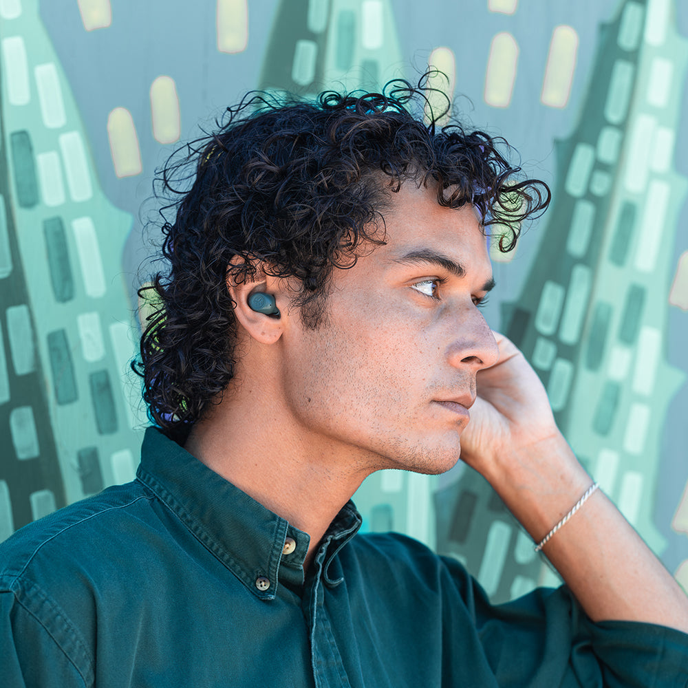 Uomo con auricolari neri, che guarda di lato. Sfondo colorato.