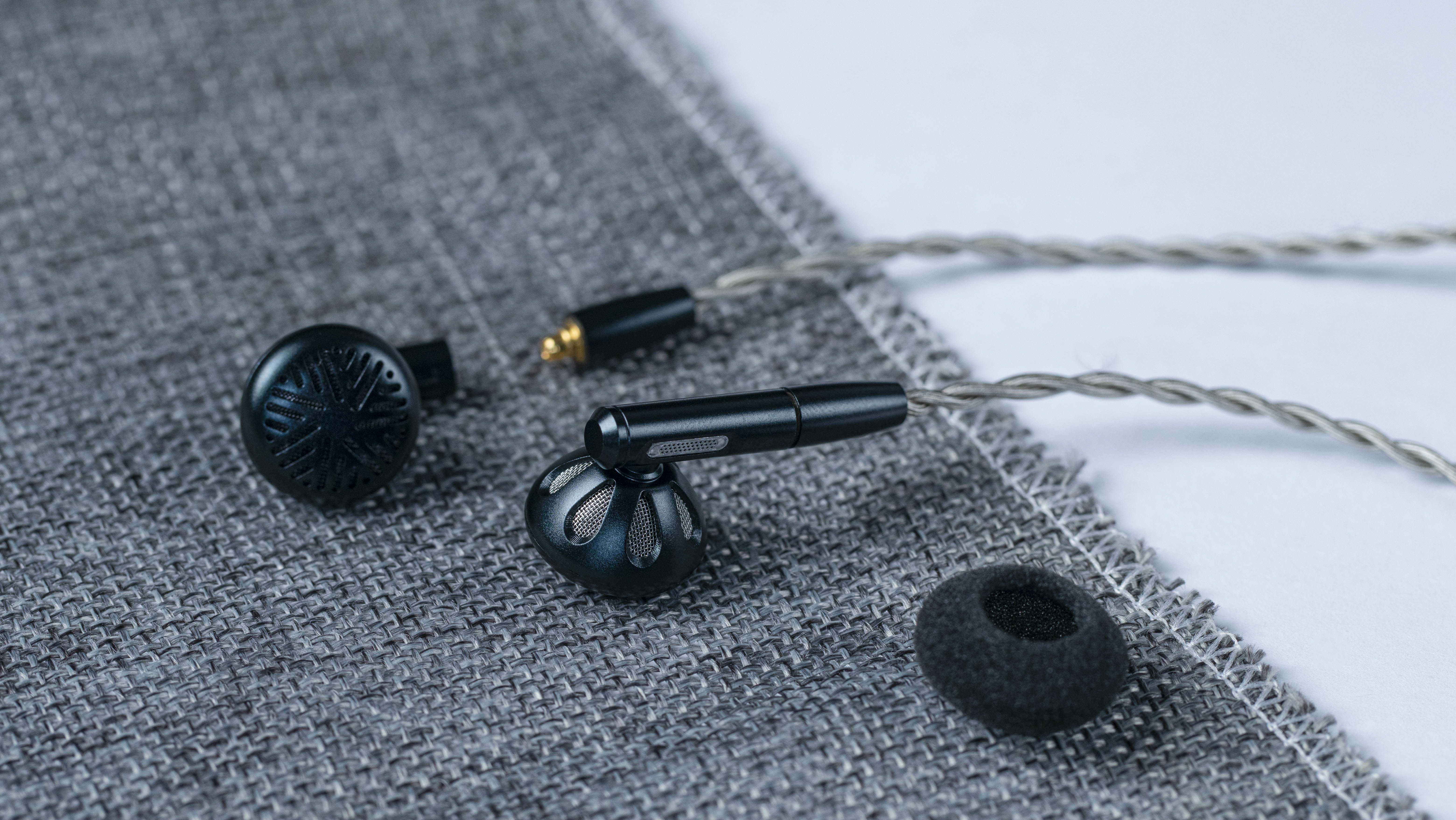 Zwarte in-ear oortelefoons, met zilveren details, en een schuimen oortip op een grijze ondergrond.