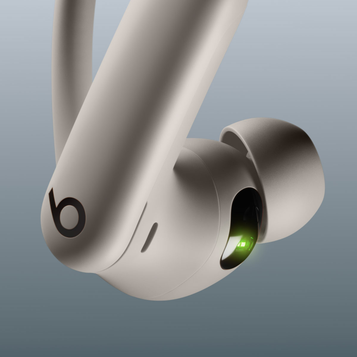 Beżowe słuchawki Beats z czarnym logo i zielonym światłem. Ujęcie z perspektywy na tle gradientu.