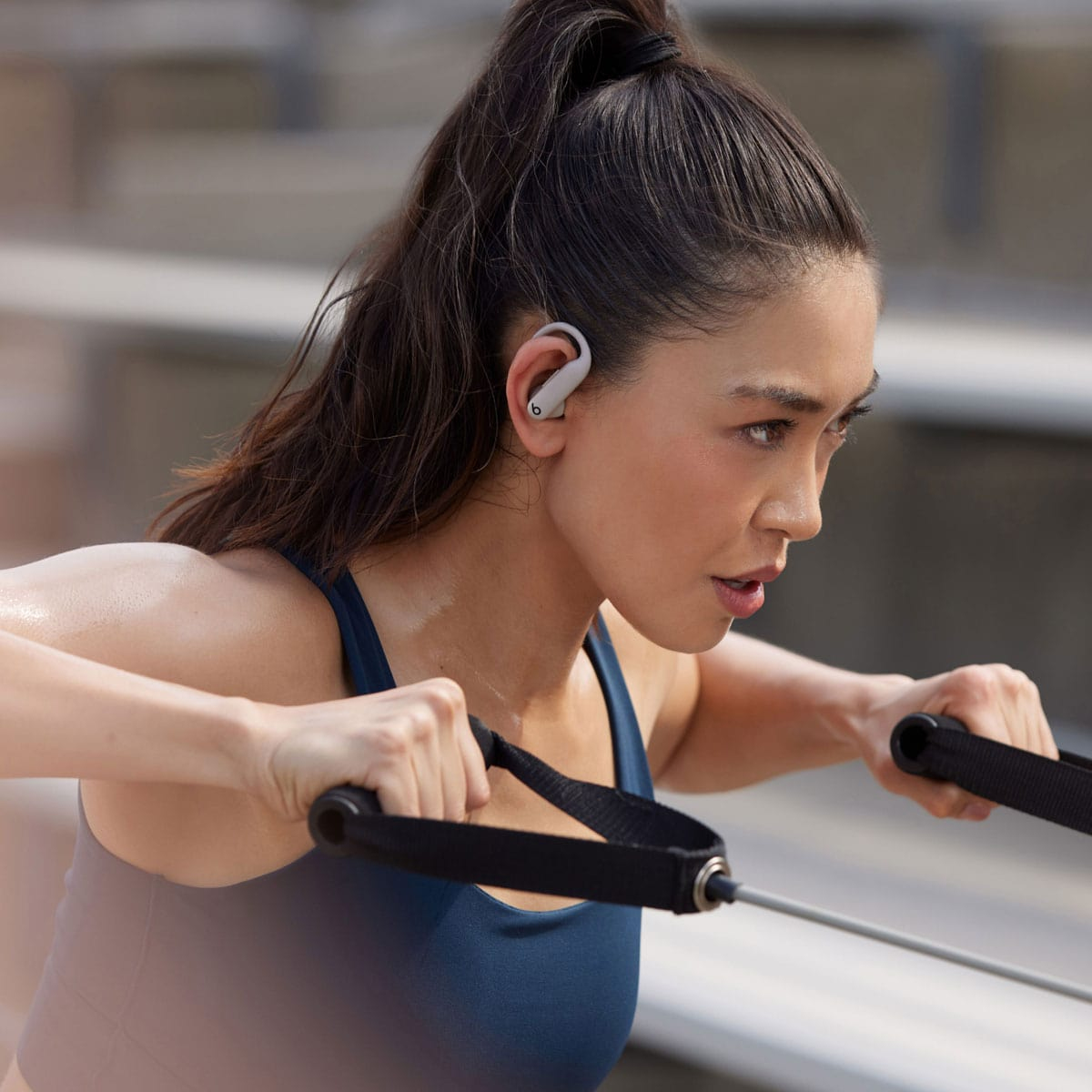 Kobieta z słuchawkami Beats ćwiczy z taśmami oporowymi. Skupiona.