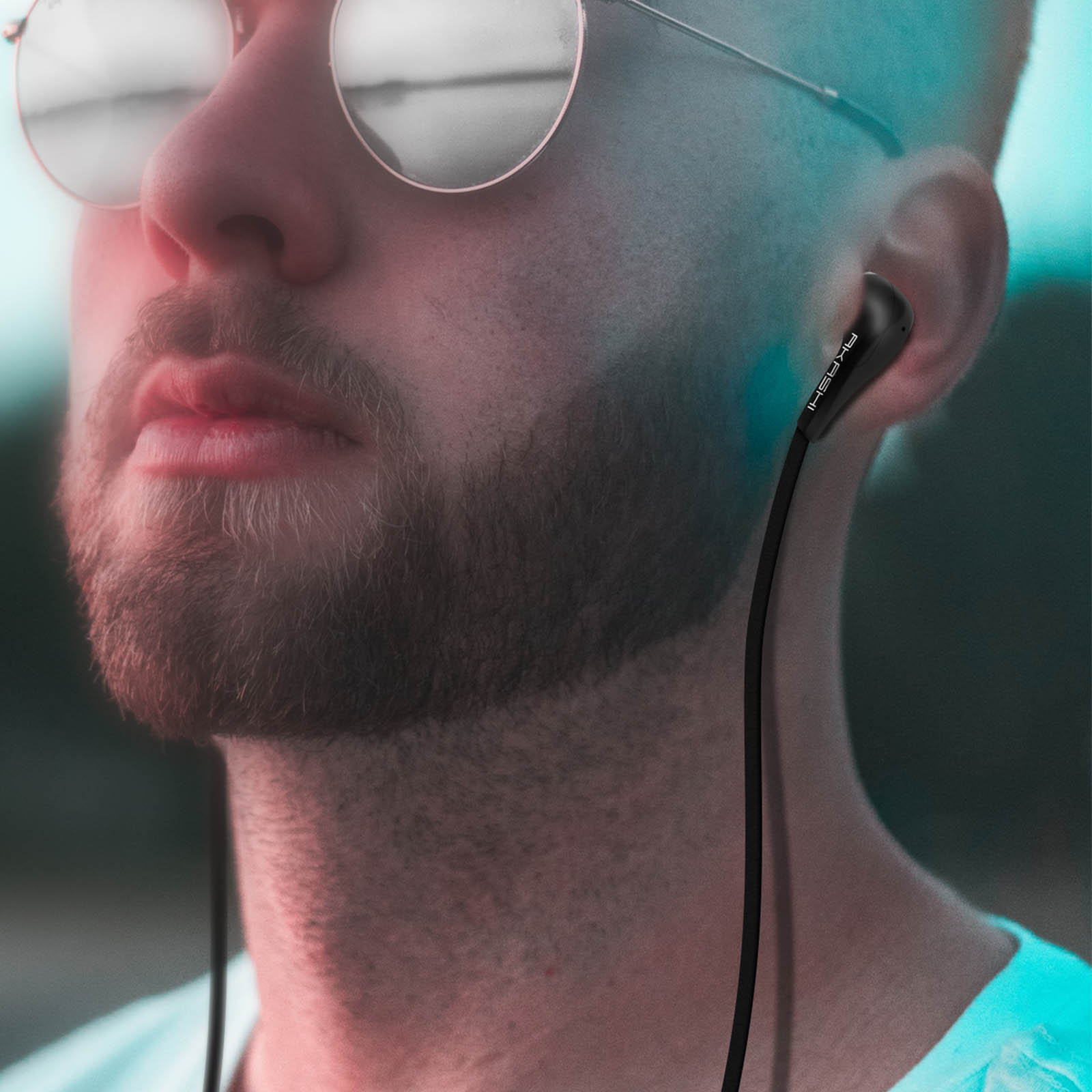 Man met zonnebril en oortelefoons. De oortelefoons zijn zwart en de man heeft een baard. De achtergrond is wazig.