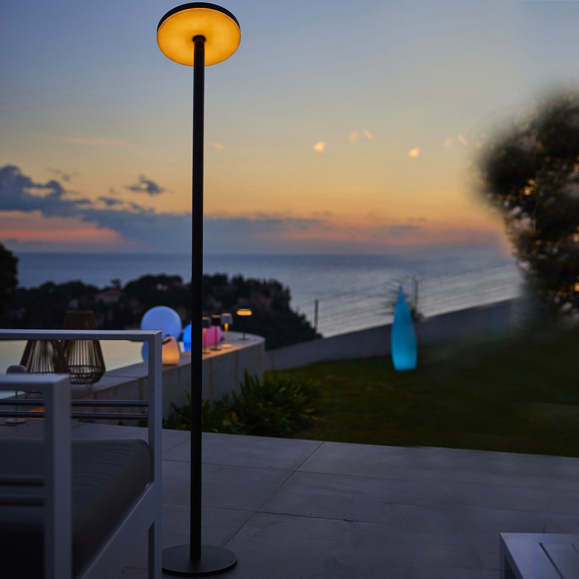 Hohe Außenlampe mit rundem Licht oben; Sonnenuntergang im Hintergrund.