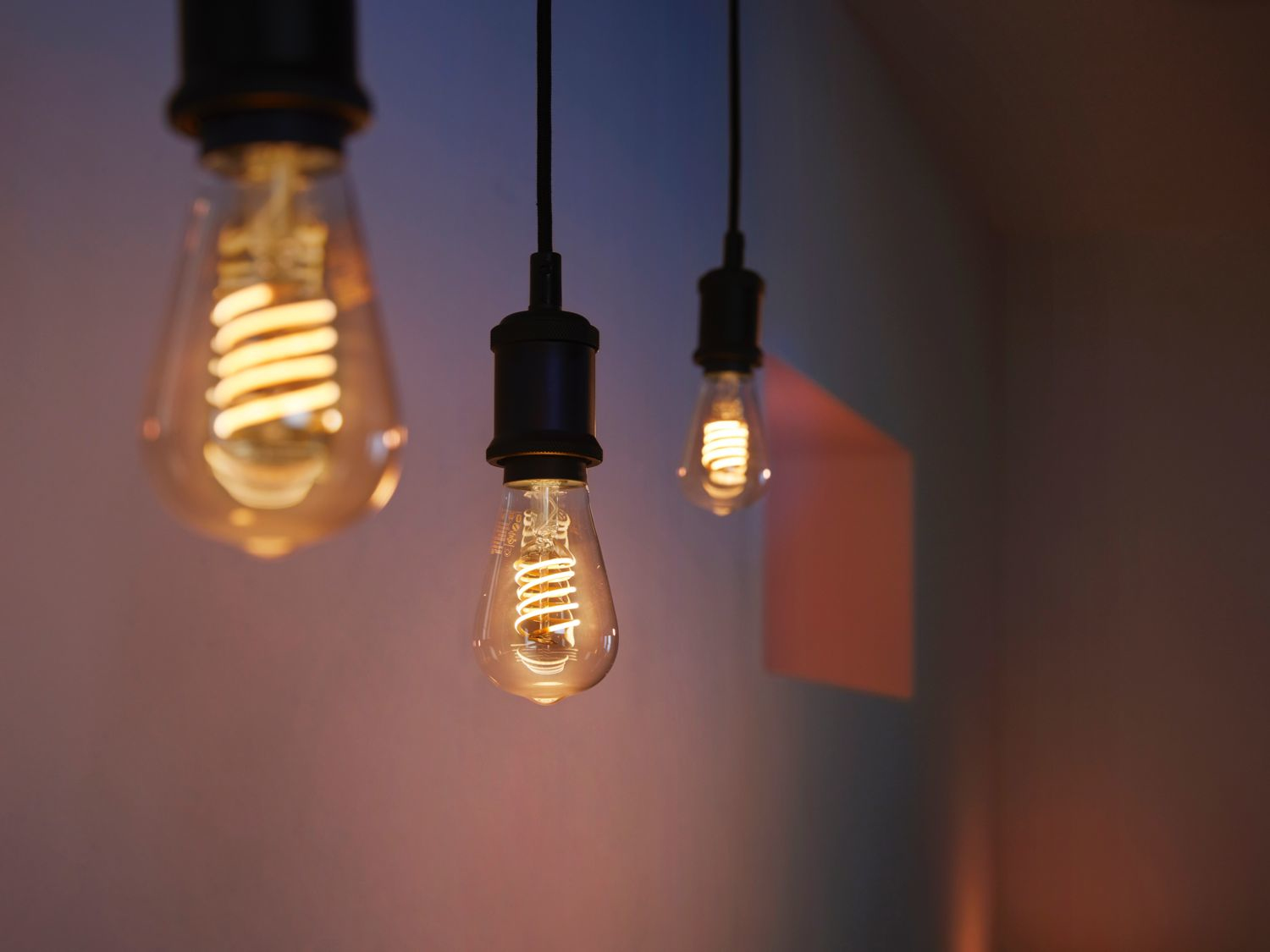 Drei Glühbirnen hängen von der Decke. Warmes Licht, dunkler Hintergrund.