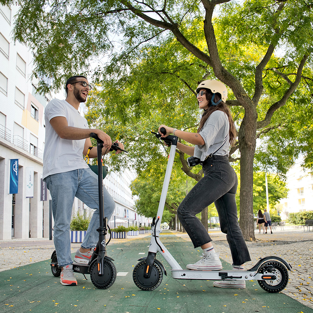 Uomo e donna con monopattini elettrici sul marciapiede, giornata di sole.