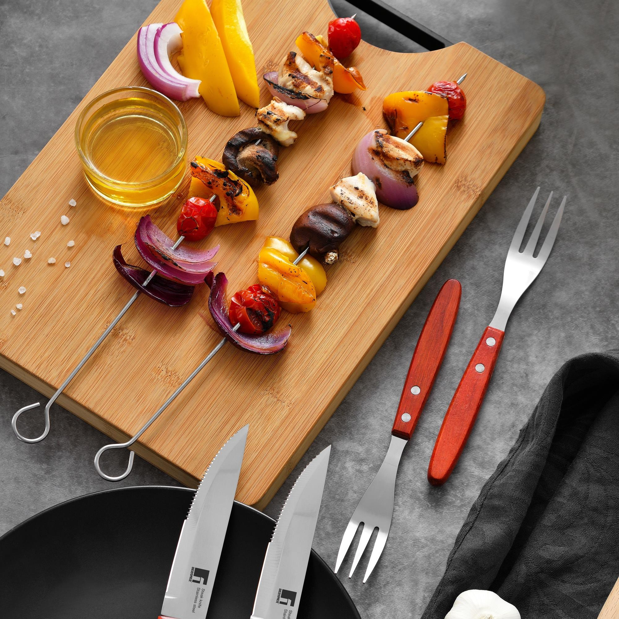 Brochetas a la parrilla, tomates, cebollas y pimientos con tenedores y cuchillos en tabla de madera.