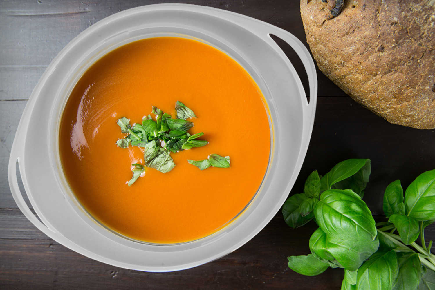 Eine Schüssel mit orangefarbener Suppe, mit Basilikum garniert, auf einem dunklen Holztisch.