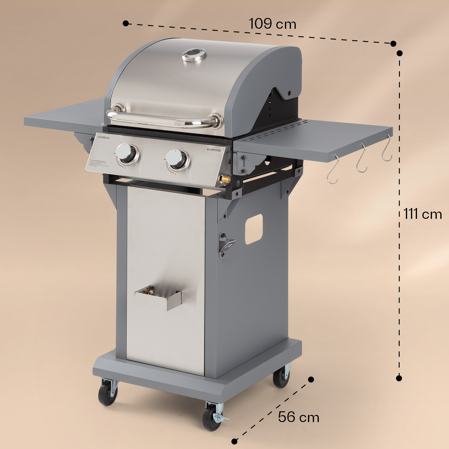 Silber-grauer Gasgrill mit Seitenablagen und einem Wagen auf Rädern, vor beigem Hintergrund.