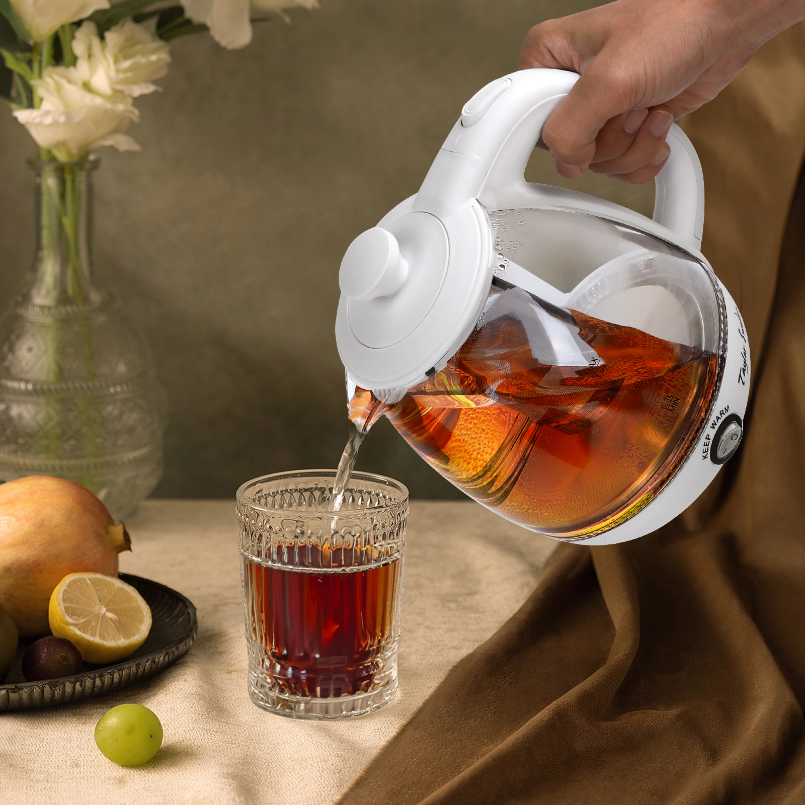 Una tetera blanca vierte té en un vaso. Hay un limón y una granada en la escena.