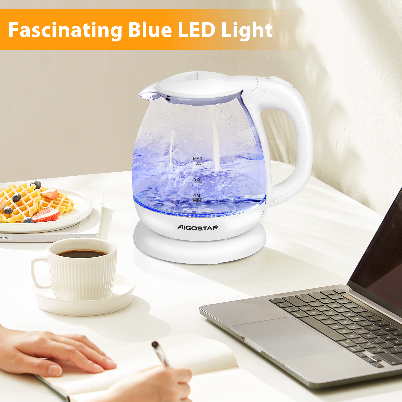 Una tetera eléctrica con luz azul, gofres, café y un portátil sobre una mesa blanca.