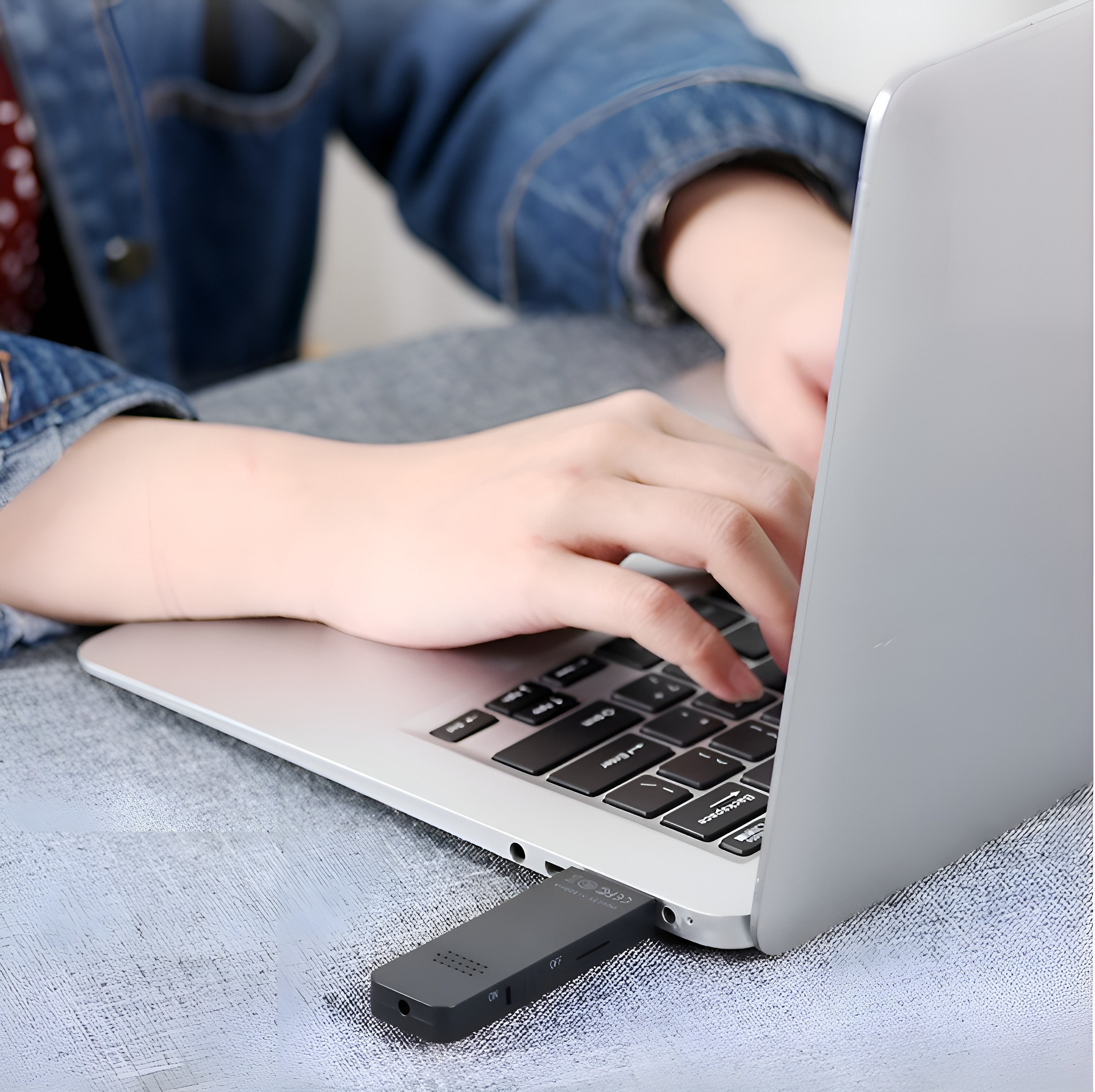Eine Person benutzt einen Laptop, an dessen Seite ein kleines, schwarzes Audiorekorder angeschlossen ist.