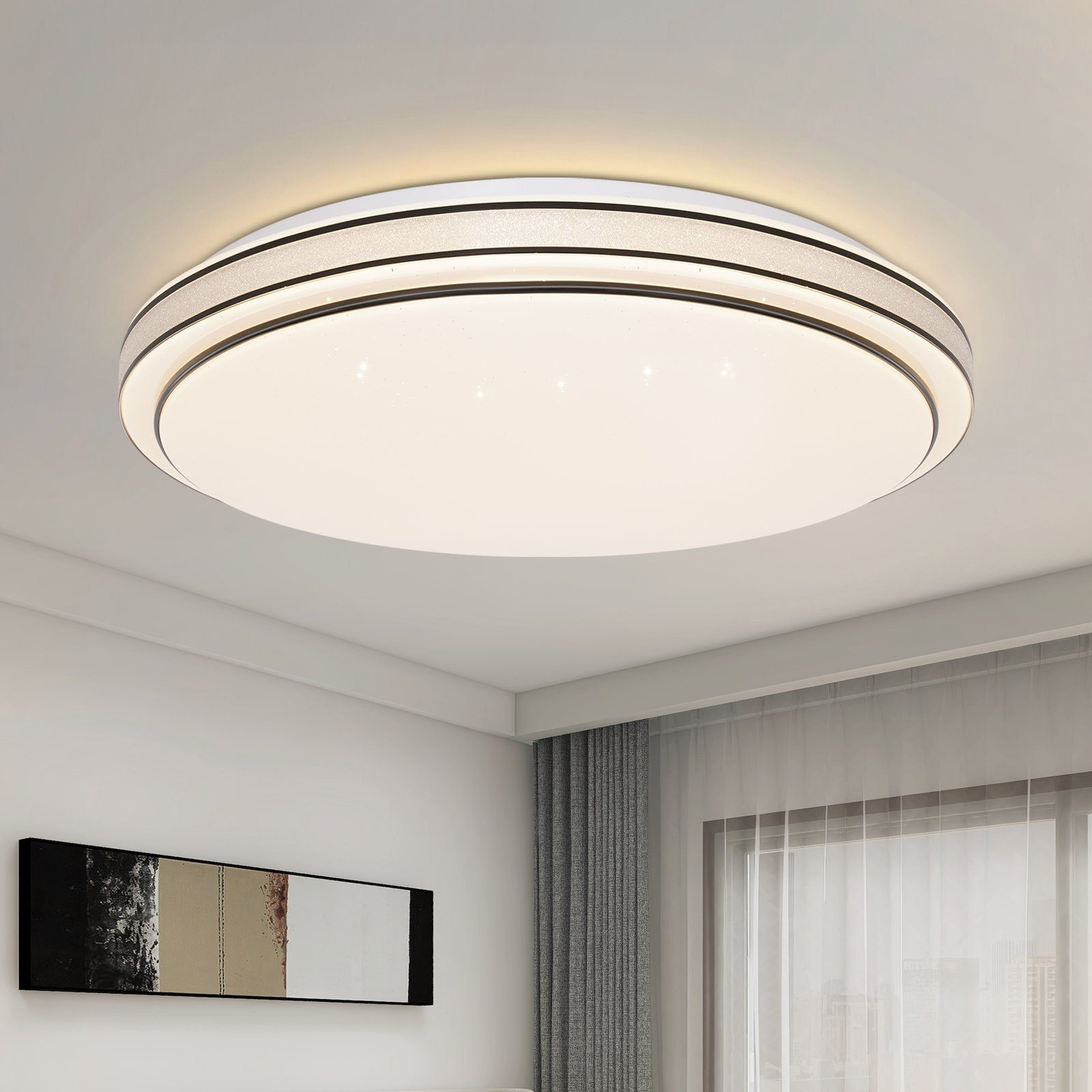 Una lámpara de techo redonda blanca con un diseño de anillo plateado y negro, sobre una habitación con un cuadro y una ventana.