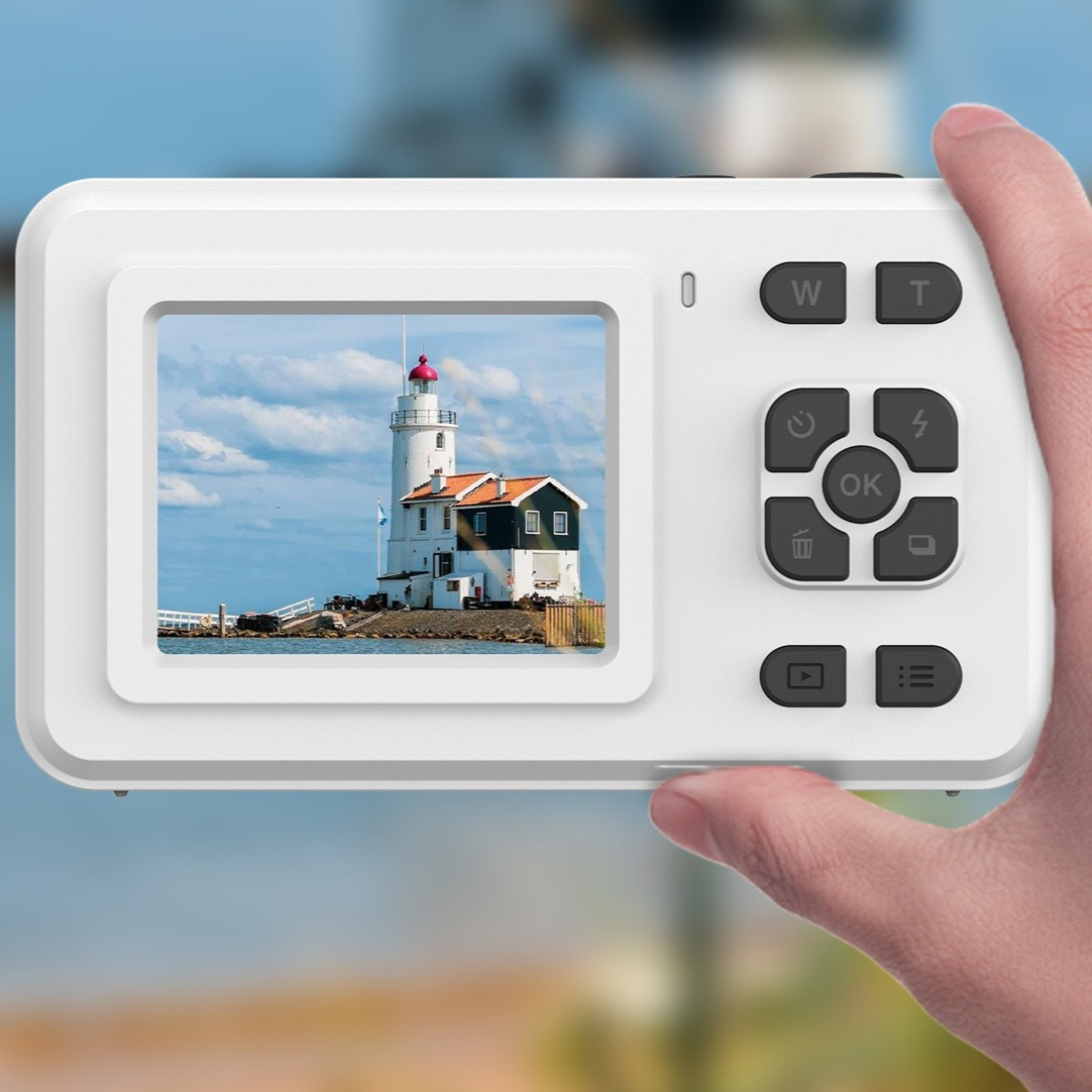 Eine Hand hält eine weiße Kamera, die einen Leuchtturm auf einer Insel zeigt. Blauer Himmel mit Wolken.