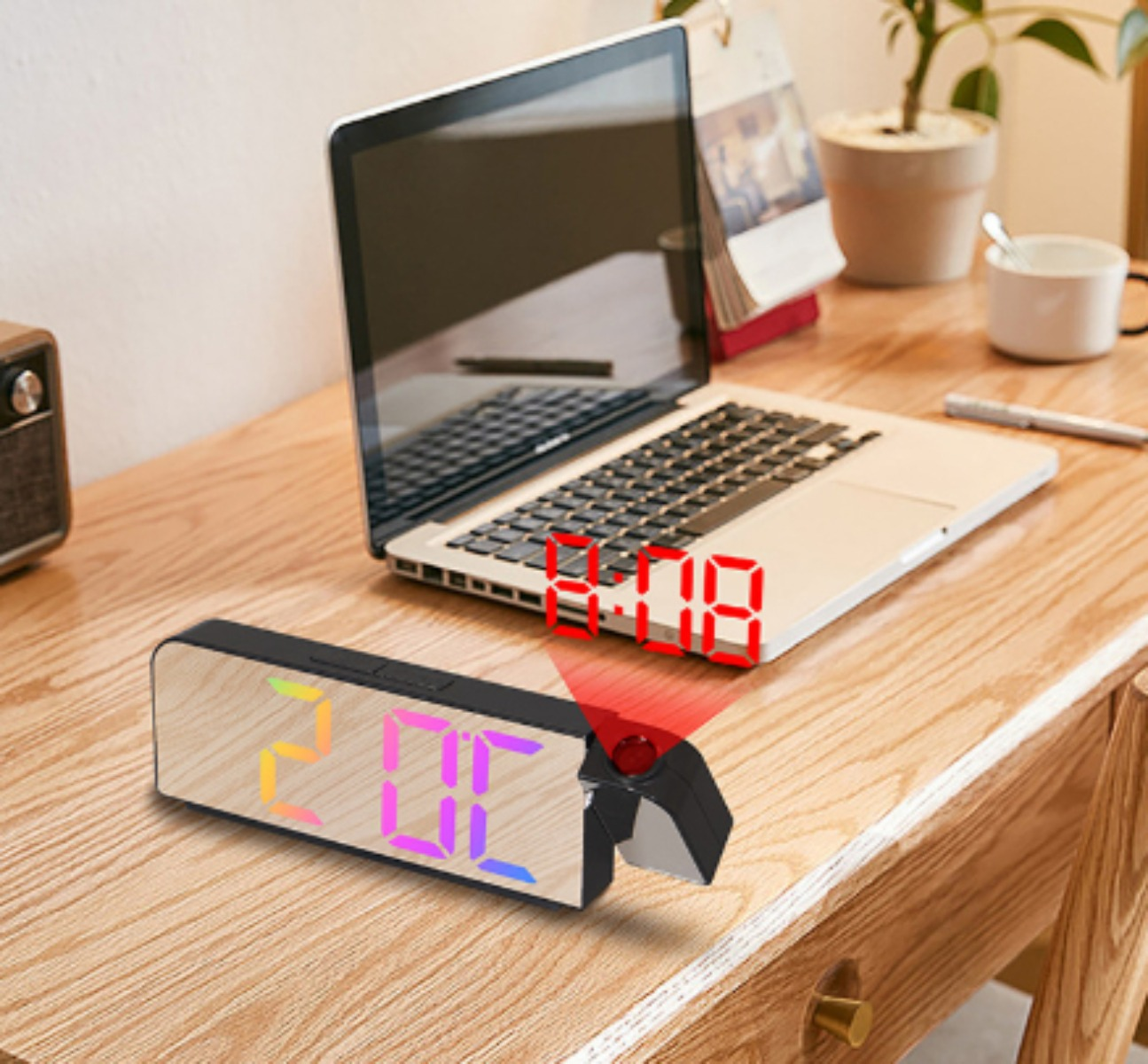 Digitaler Wecker, der die Zeit projiziert. Zeigt rote Ziffern, mit Laptop und anderen Gegenständen auf einem Schreibtisch.