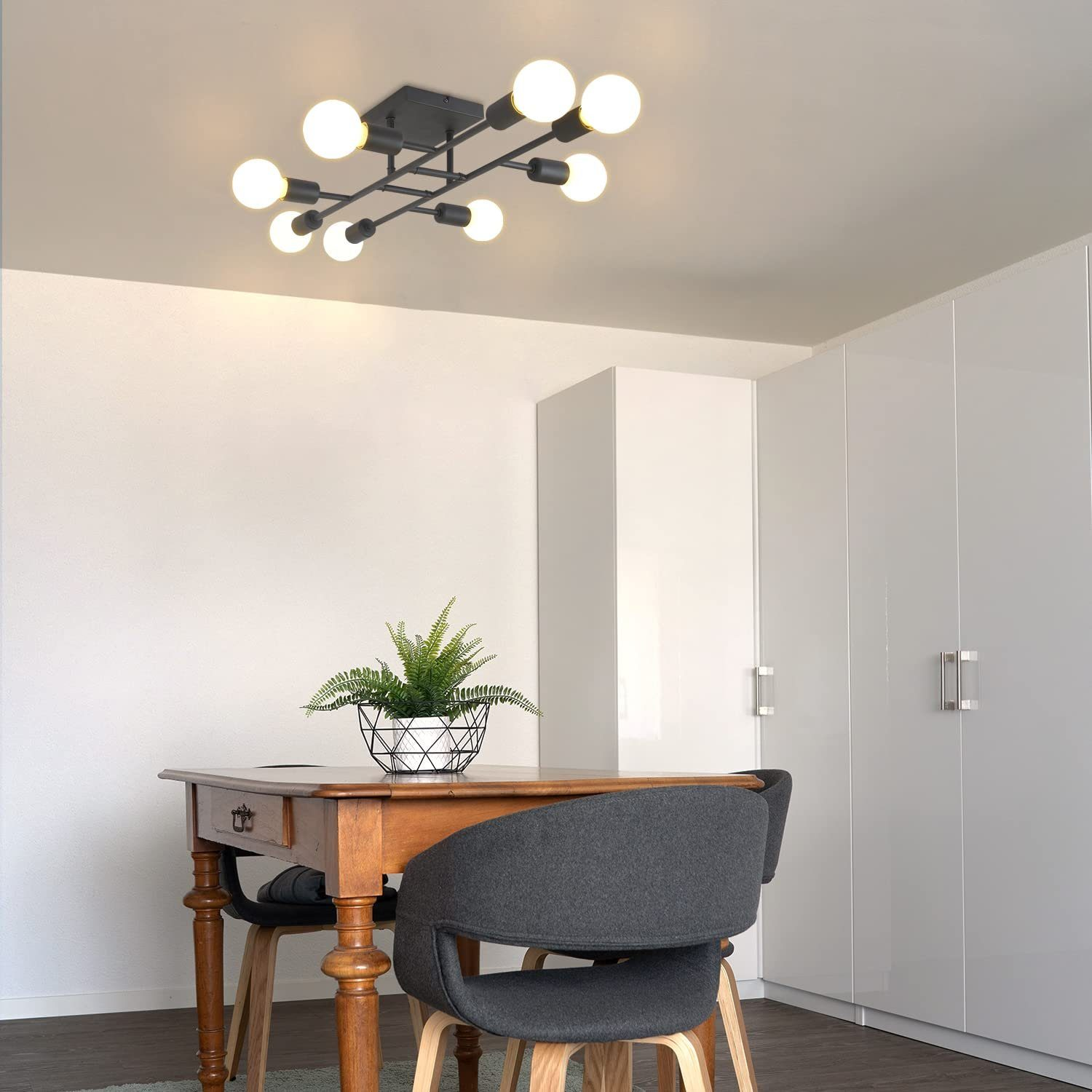 Un comedor con mesa de madera, sillas y lámpara de techo. Armarios blancos a la derecha.