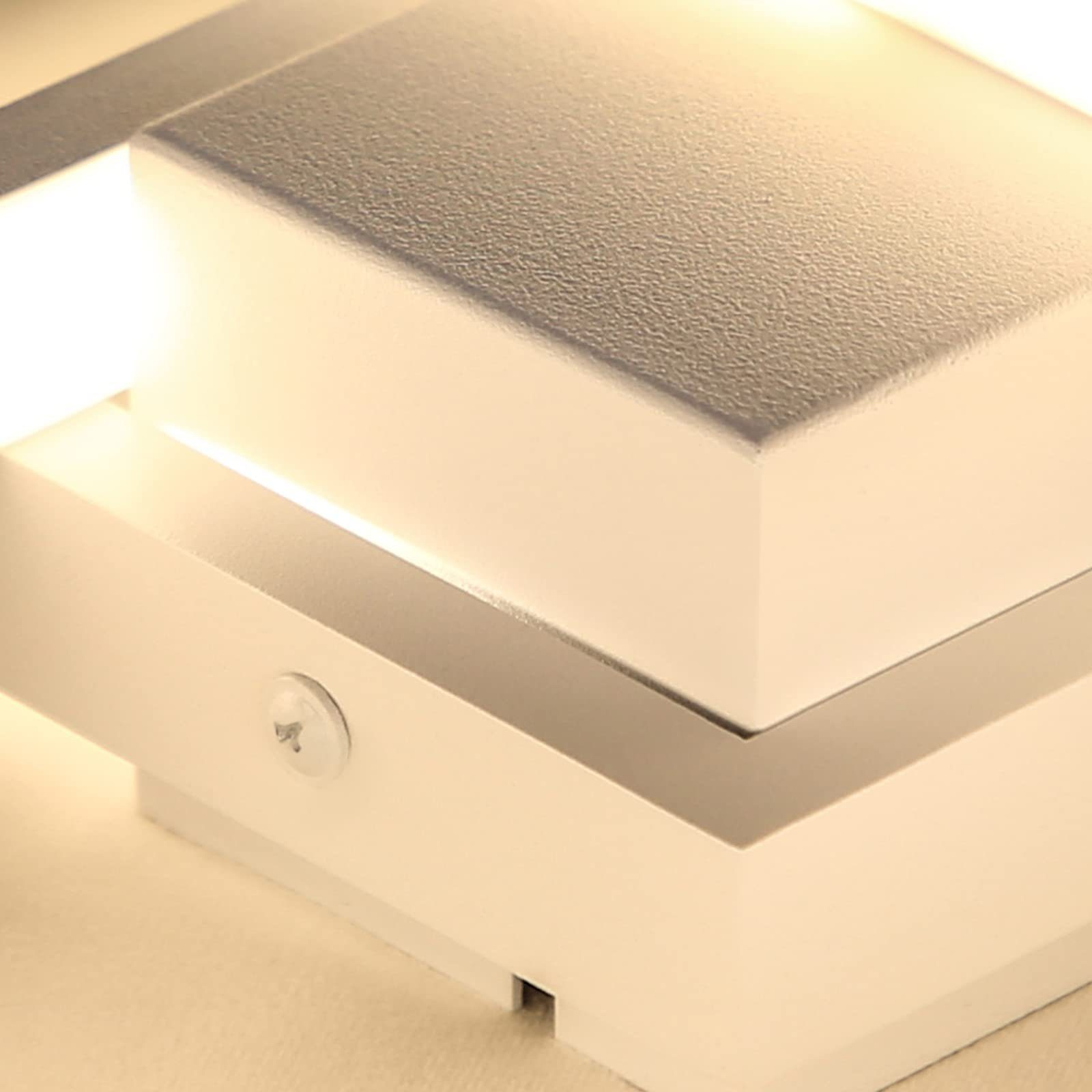 Zbliżenie białej lampy ściennej, o prostym designie i jasnym świetle emitowanym przez oprawę.